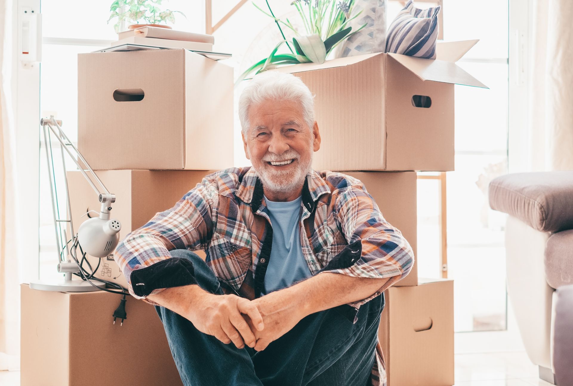 An elderly man is sitting on the floor in front of a pile of cardboard boxes.