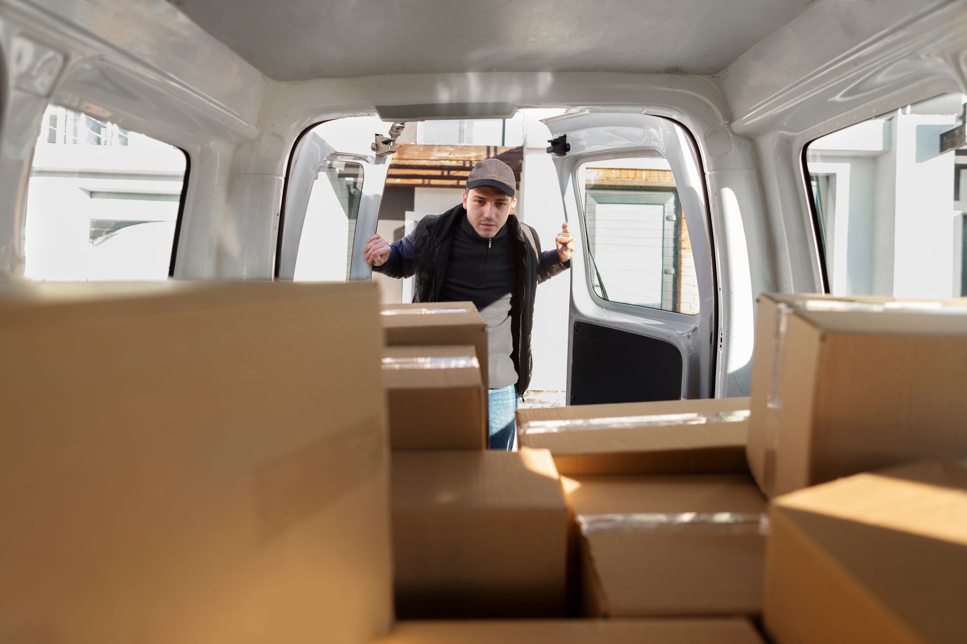 A delivery man is standing in the back of a van filled with cardboard boxes.