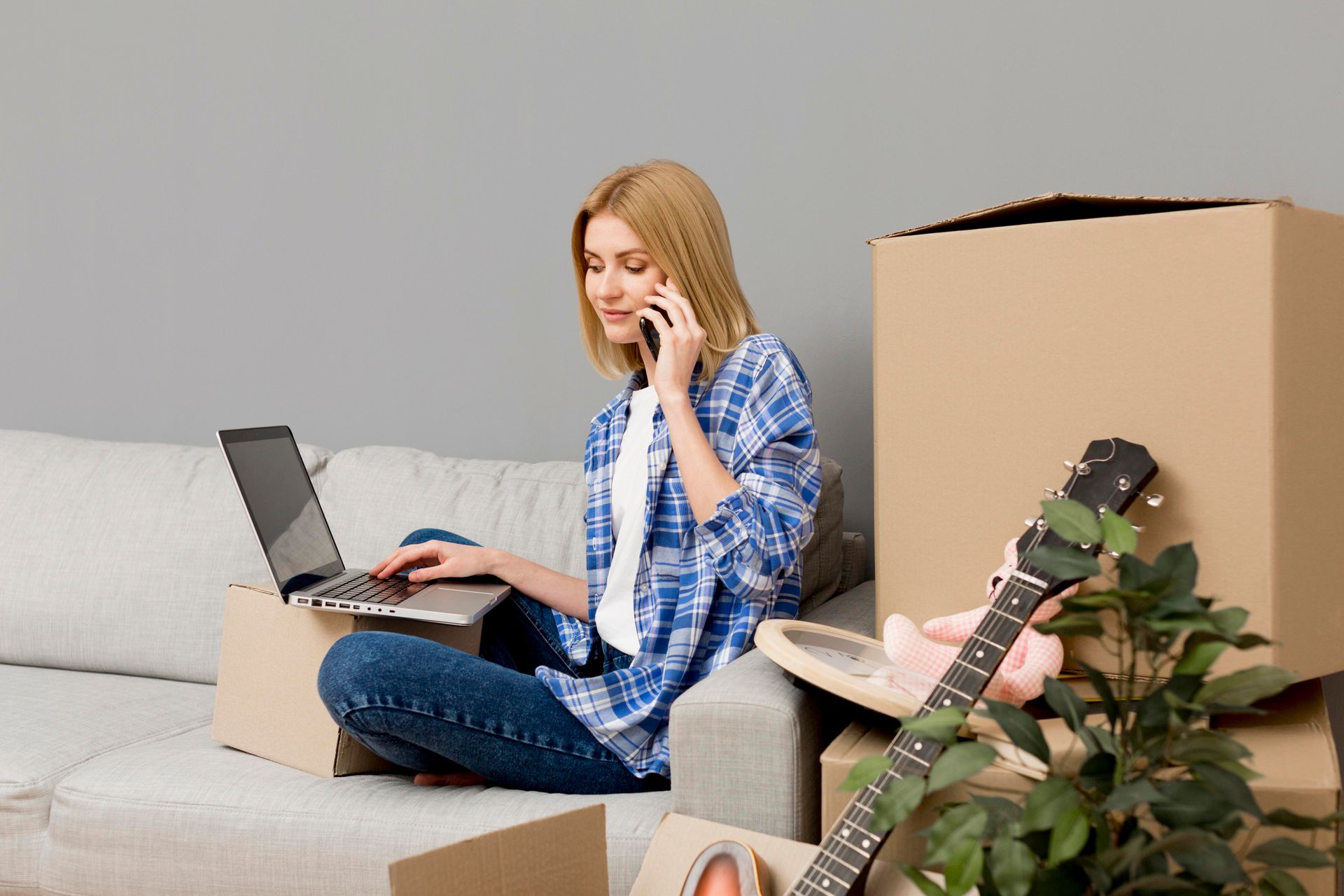 A woman is sitting on a couch using a laptop and talking on a cell phone.
