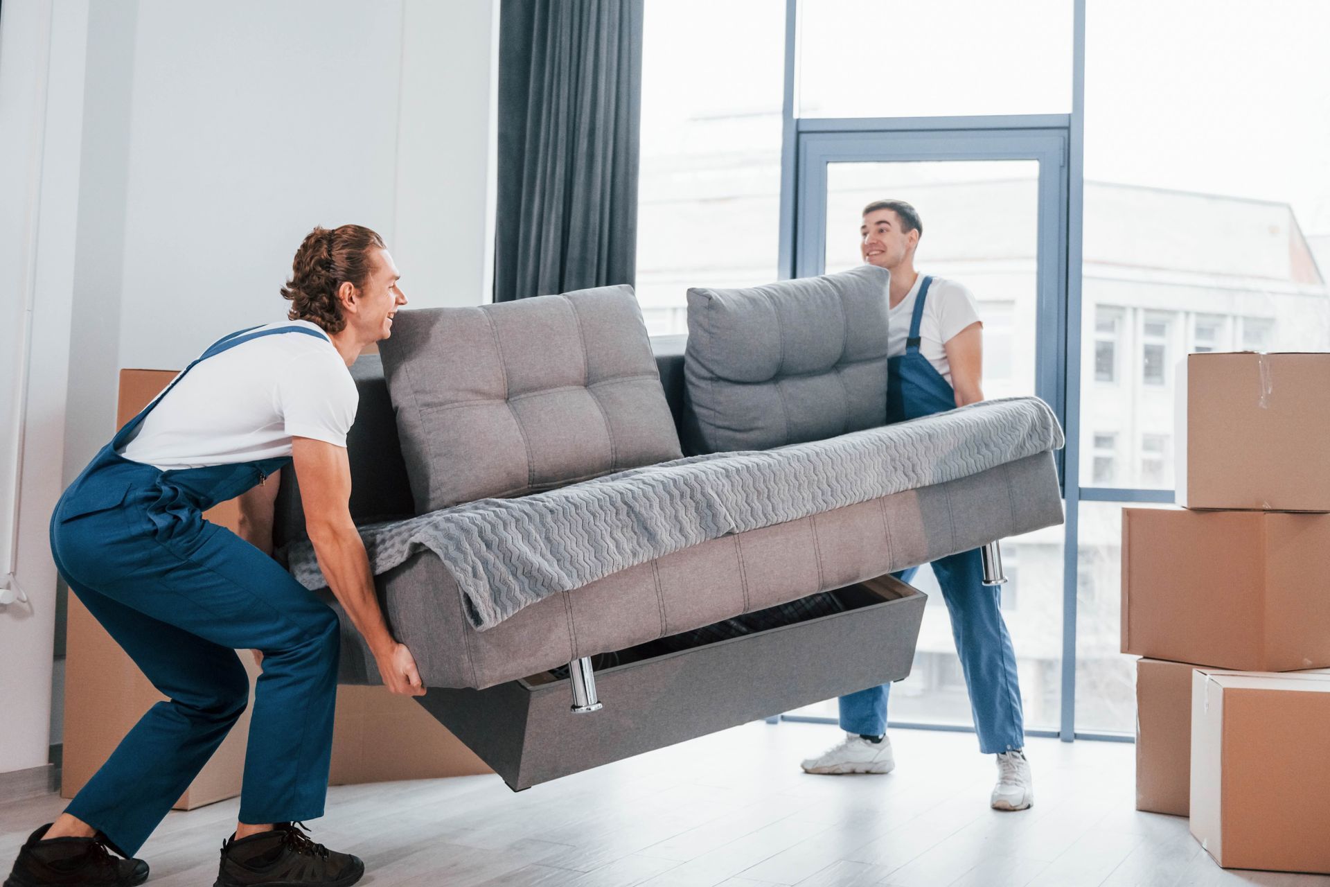 Two men are carrying a couch in a living room.