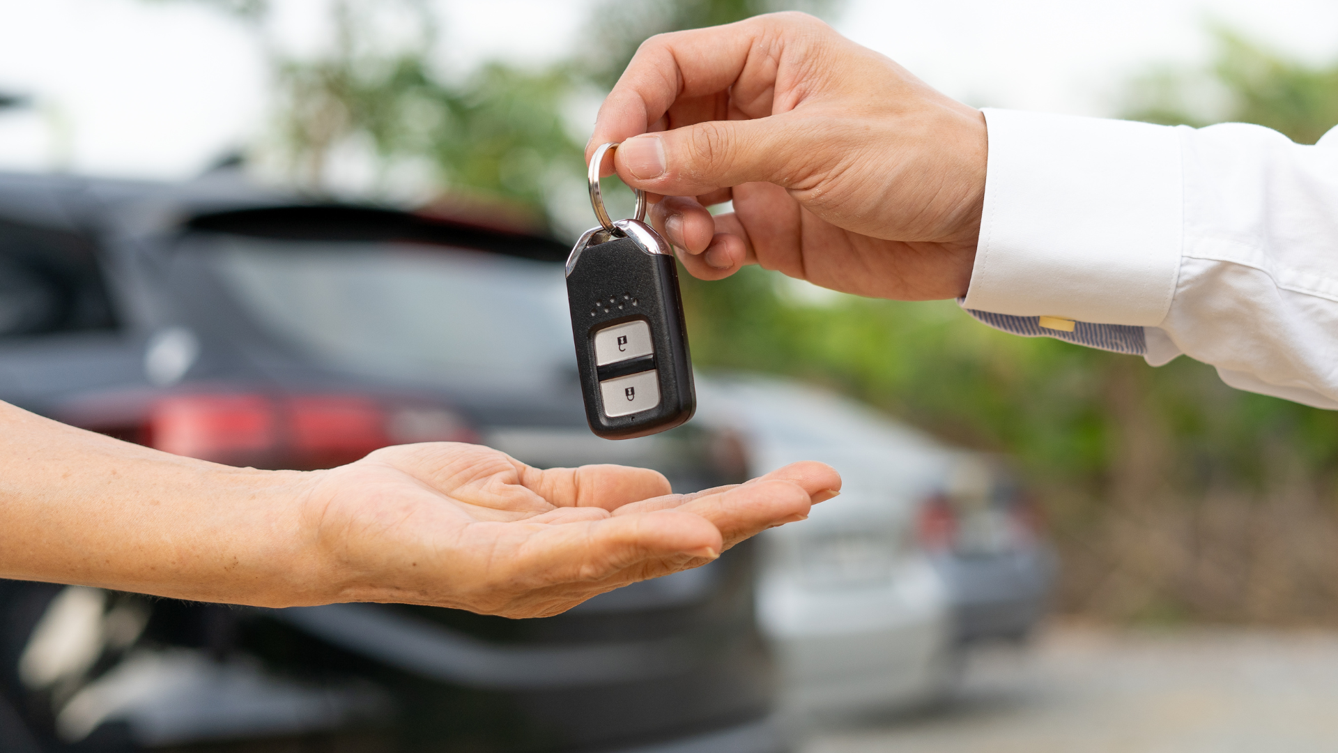 A man is handing a car key to another man in front of a car.