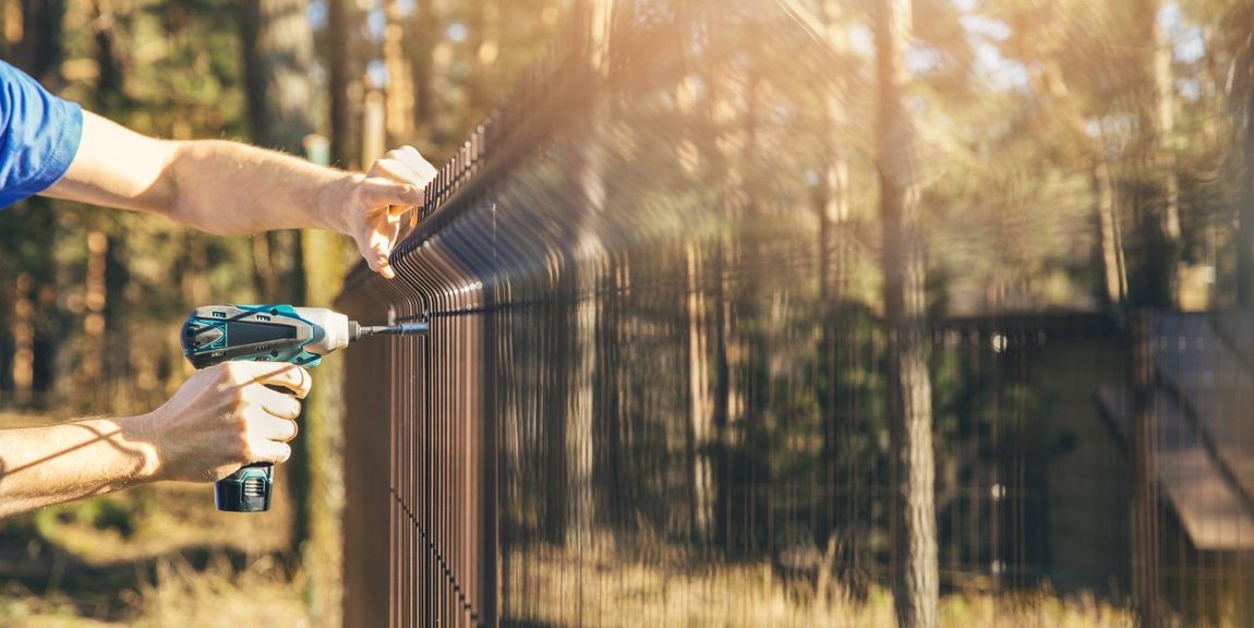 A man is using a drill to install a fence in the woods.