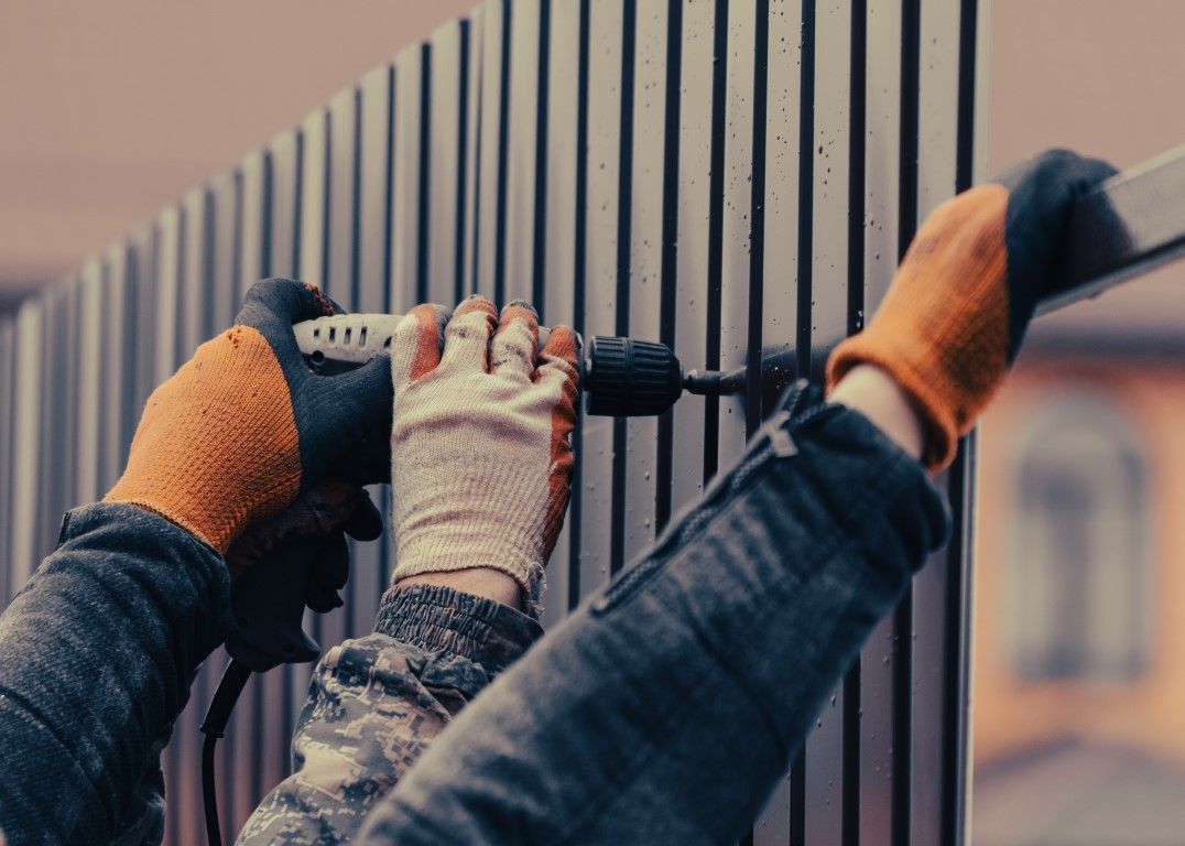 A person is drilling a hole in a fence with a drill.