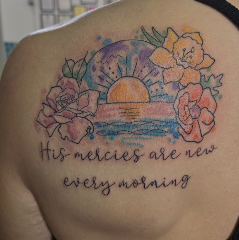Watercolor tattoo on a shoulder. Flowers, sunrise over water, and the words, 