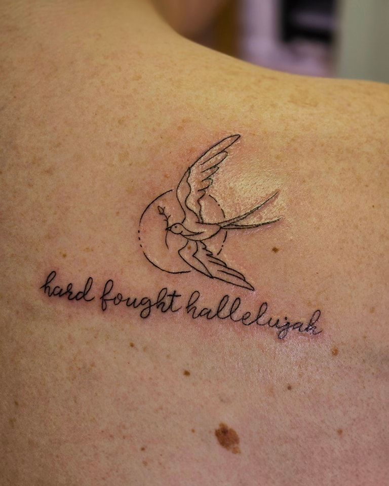 Tattoo of a swallow in flight in front of a circle with the words 