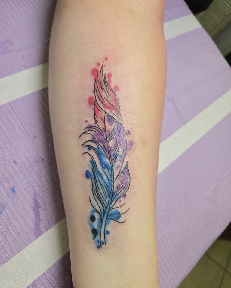 Watercolor feather tattoo on an arm, featuring pink, purple, and blue hues.