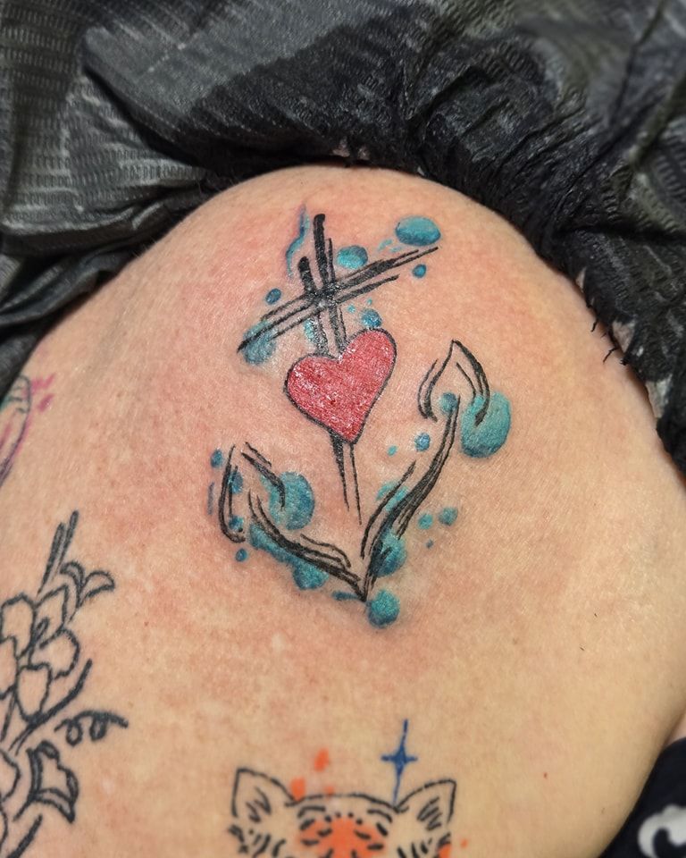 Anchor tattoo with a red heart, teal splashes, and black outline on skin.