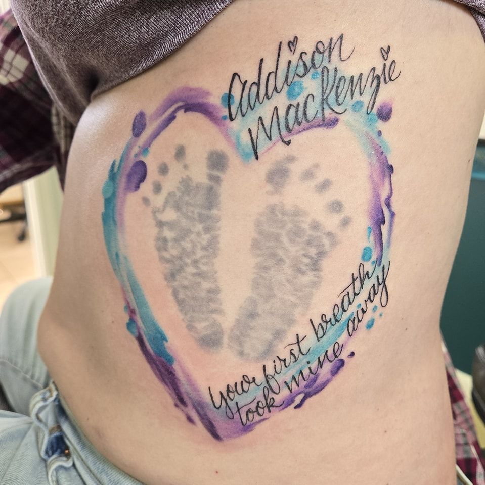 Tattoo of baby footprints inside a heart with watercolor effect; names 