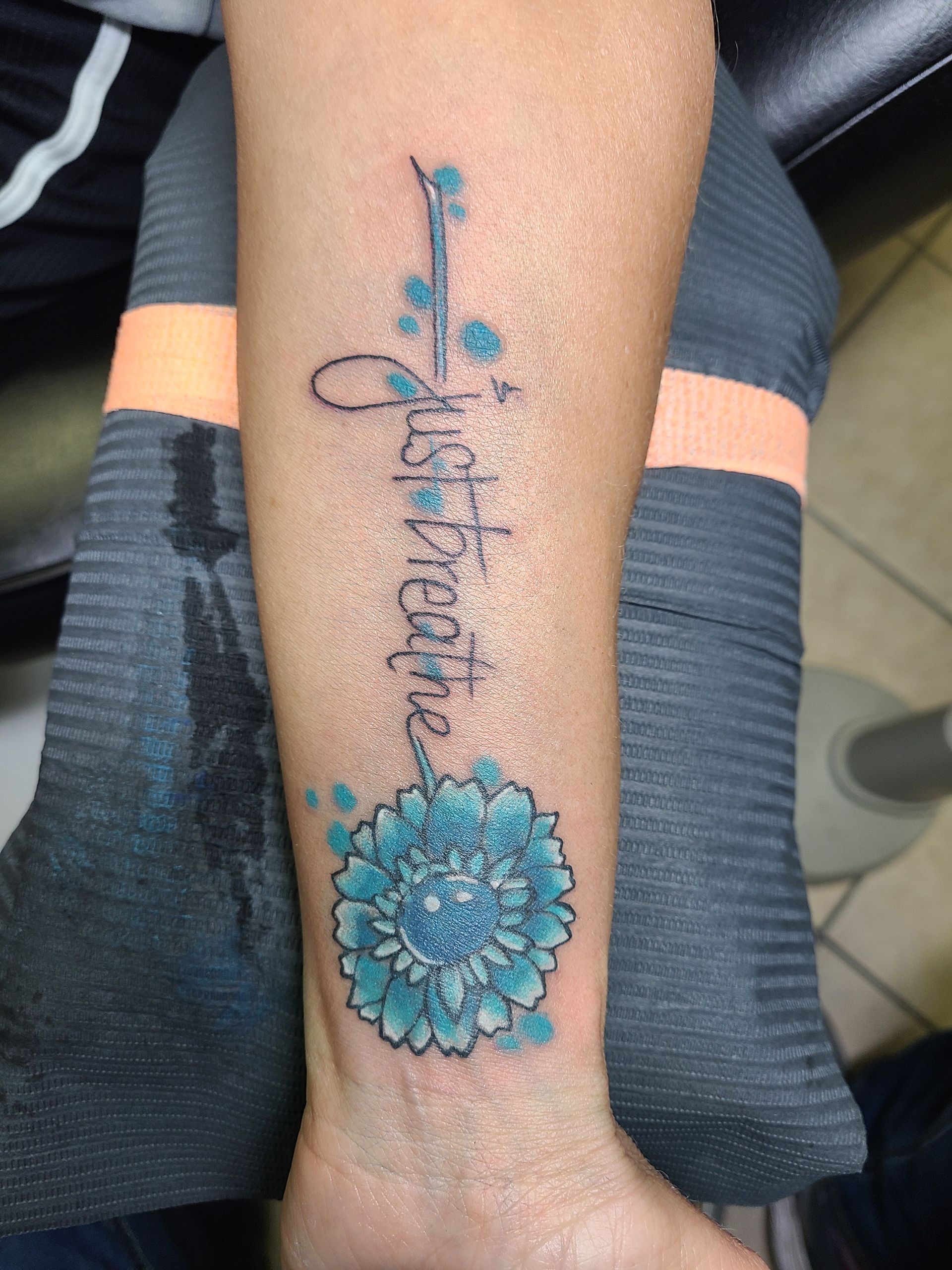 A person has a tattoo on their arm that says just breathe