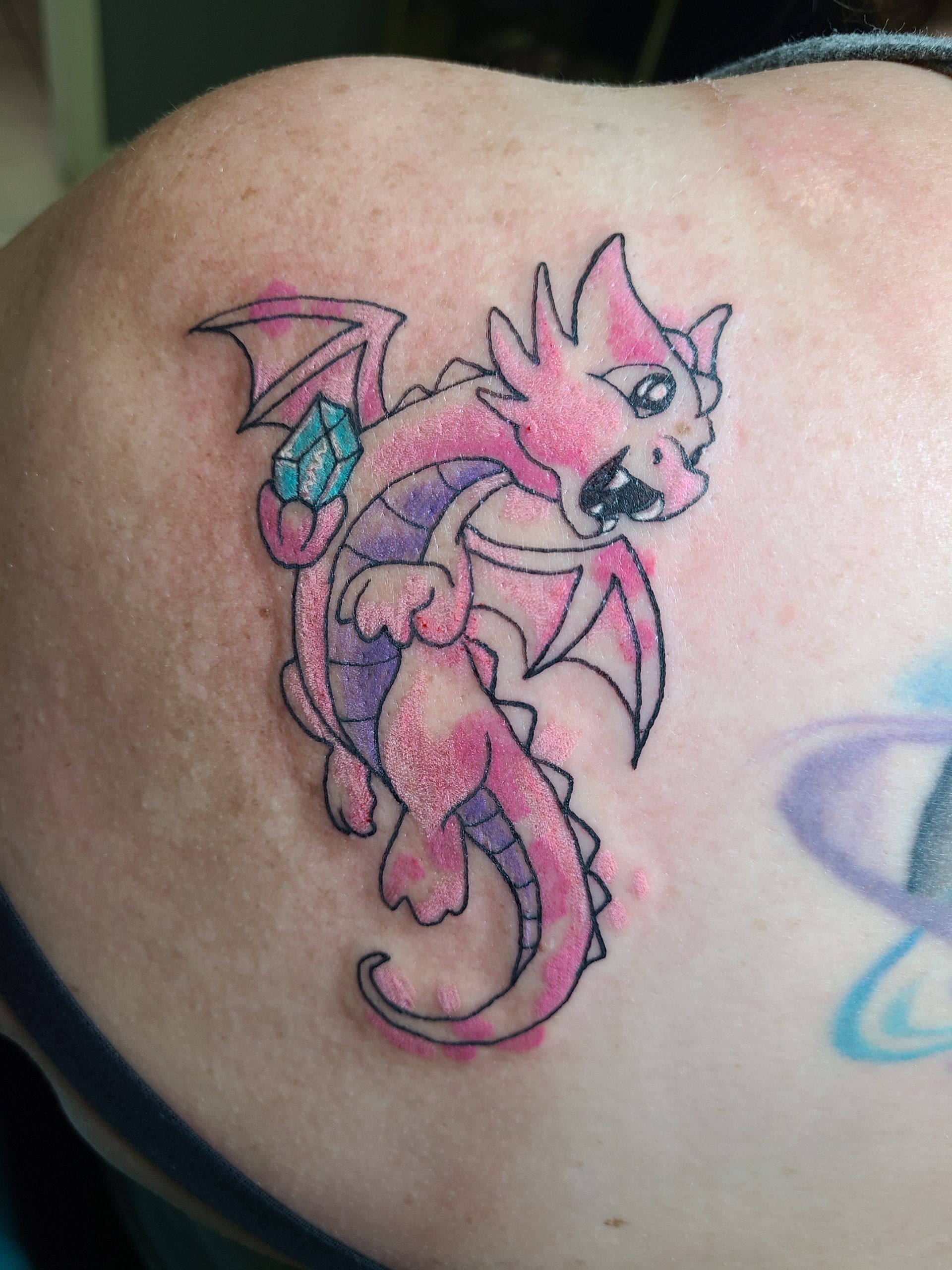 A woman has a pink and purple dragon tattoo on her back