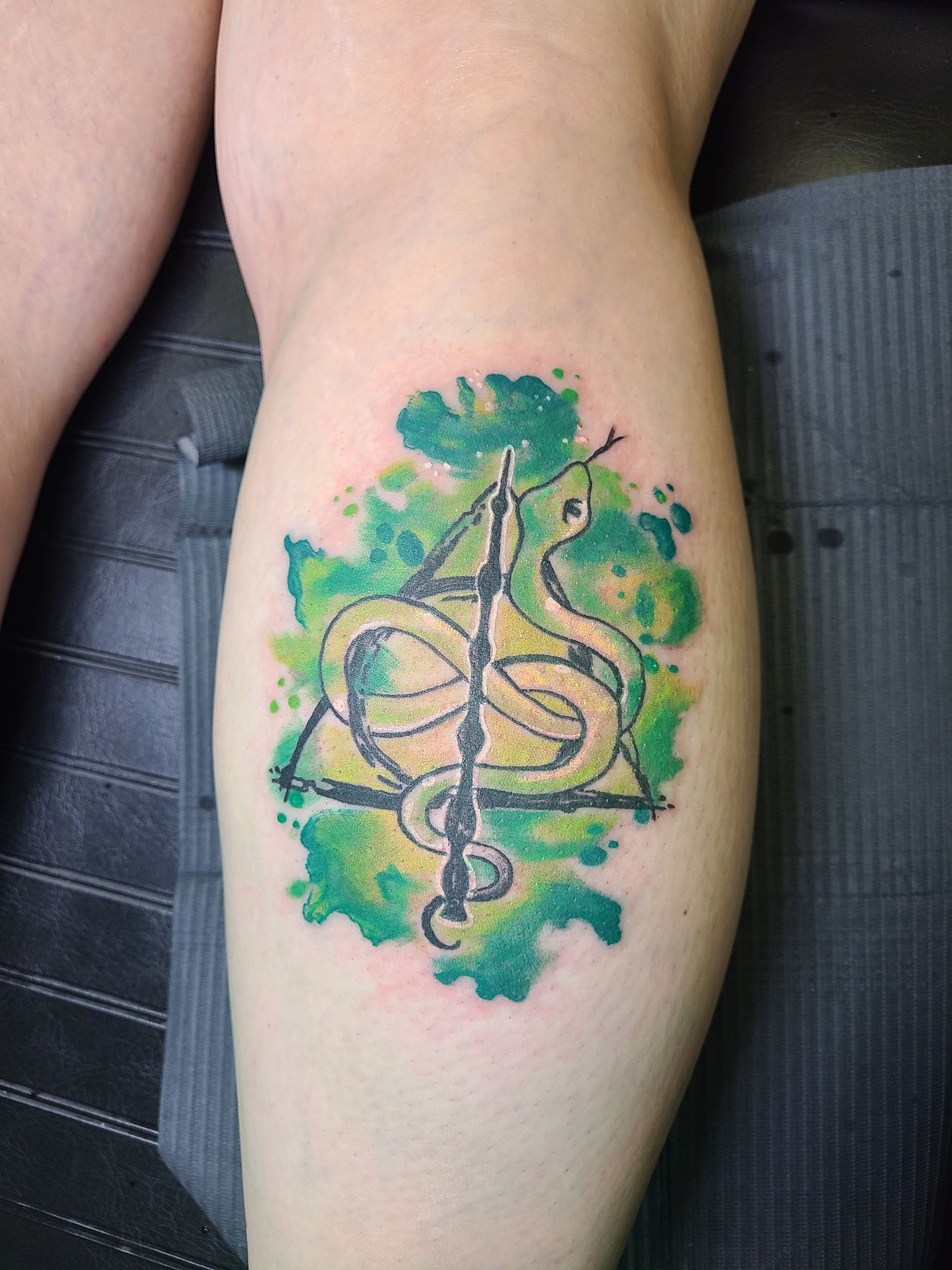 A person has a tattoo of a snake and a wand on their leg.