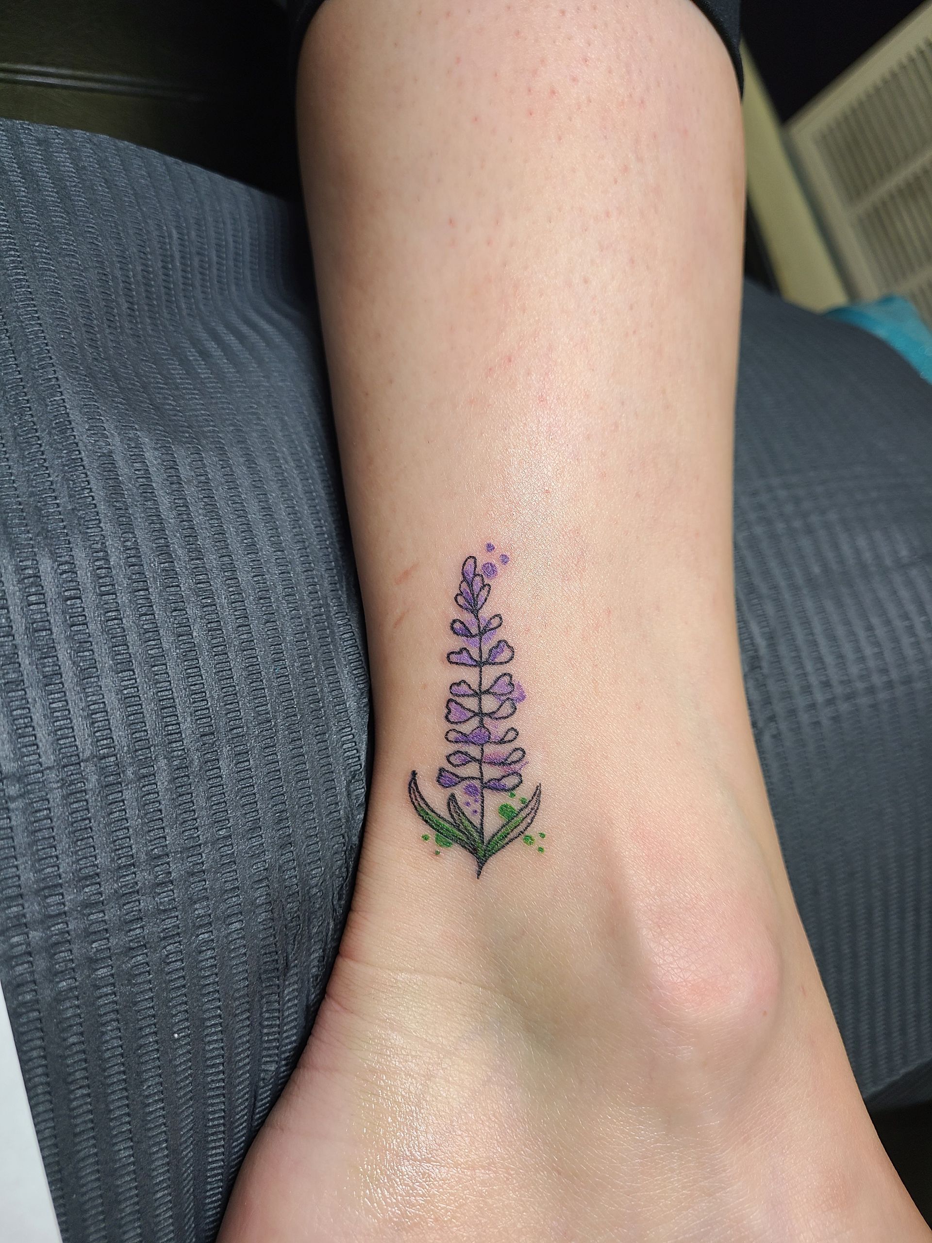 A person has a small purple flower tattoo on their ankle.