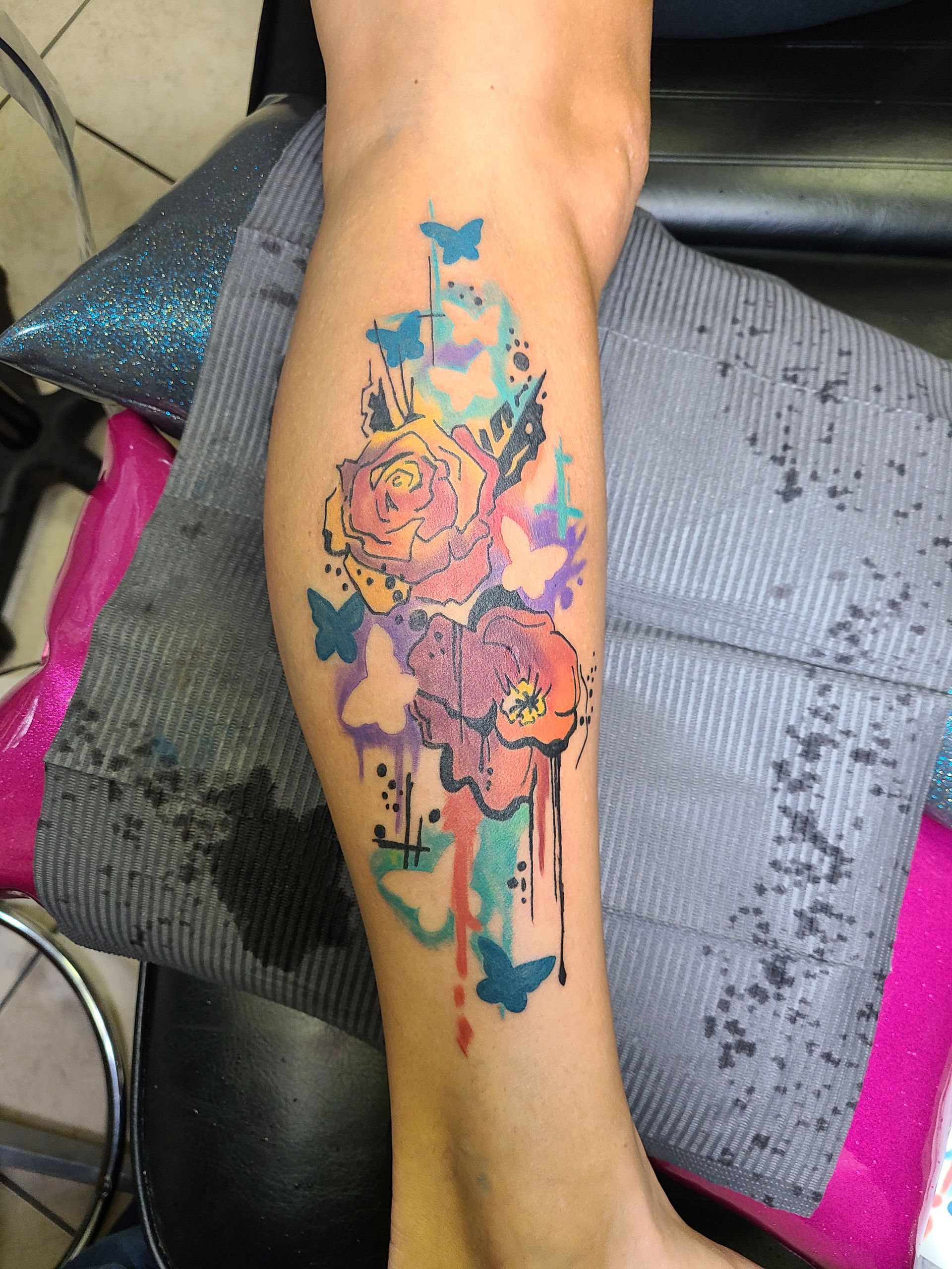 A woman has a colorful tattoo of flowers and butterflies on her leg