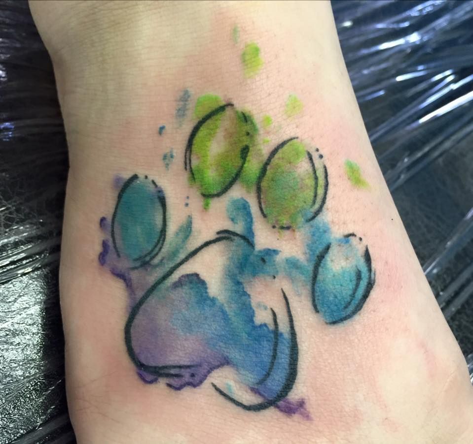 A person has a watercolor paw print tattoo on their wrist