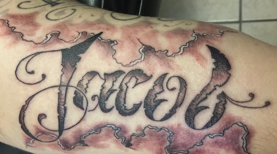 A person has a tattoo of the name jacob on their arm.