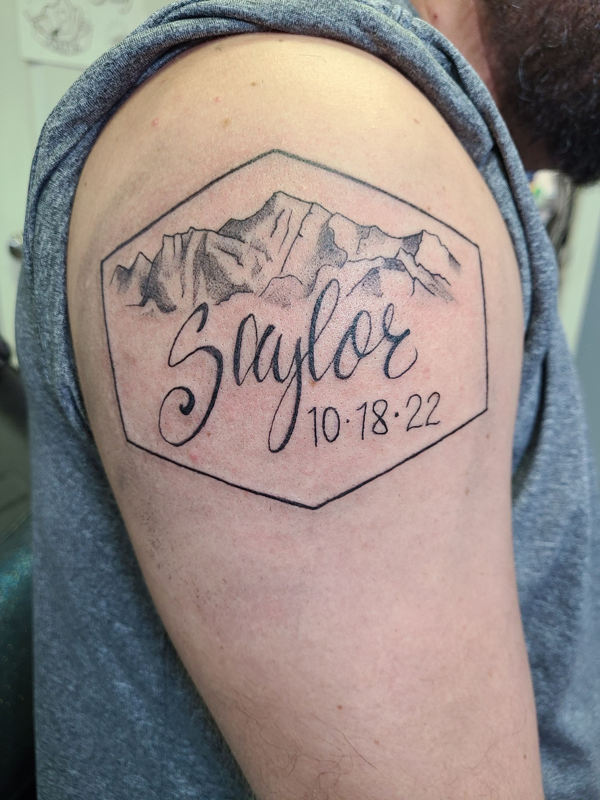 A man has a tattoo of a mountain and the name saylor on his shoulder.