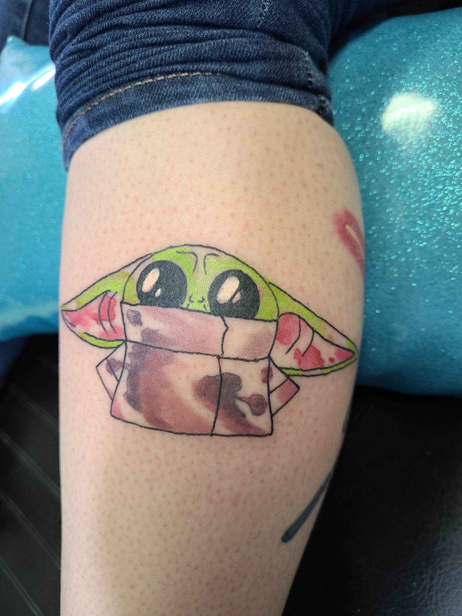 A person has a tattoo of a baby yoda on their leg.