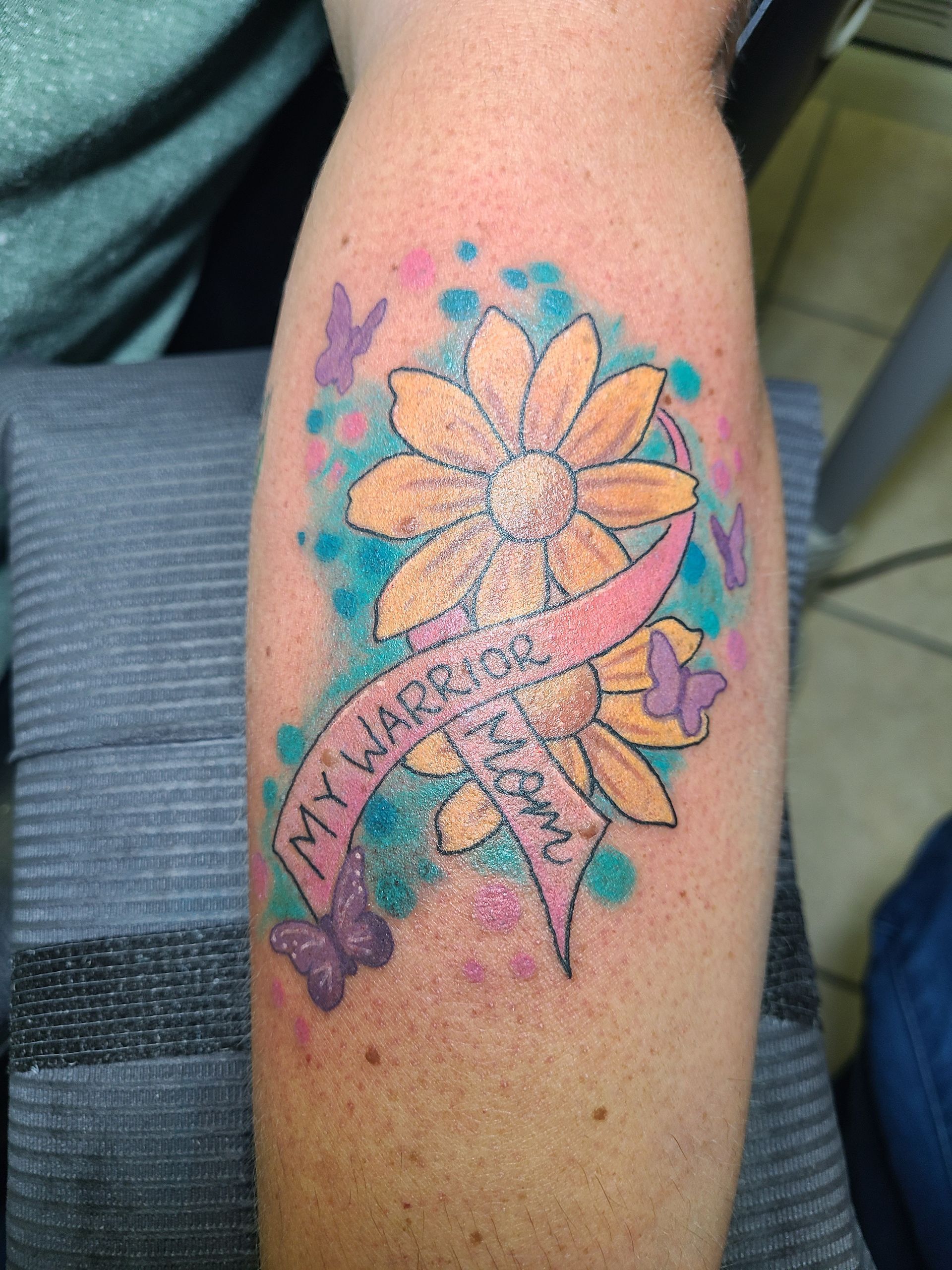 A woman has a tattoo of a flower with a pink ribbon that says my heart is yours