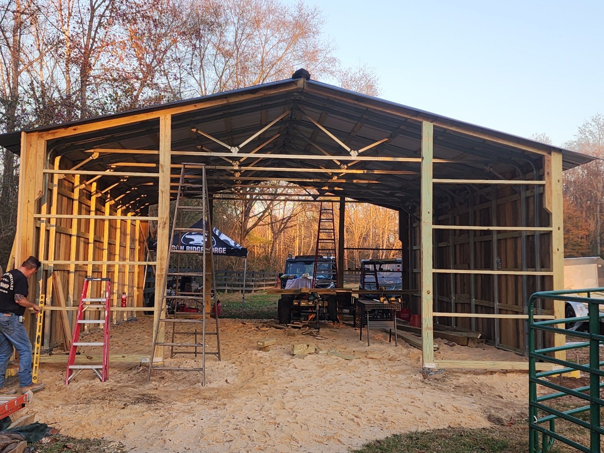 Construction of a large, open-air shed. Wooden frame with metal roof, sawdust on the ground.