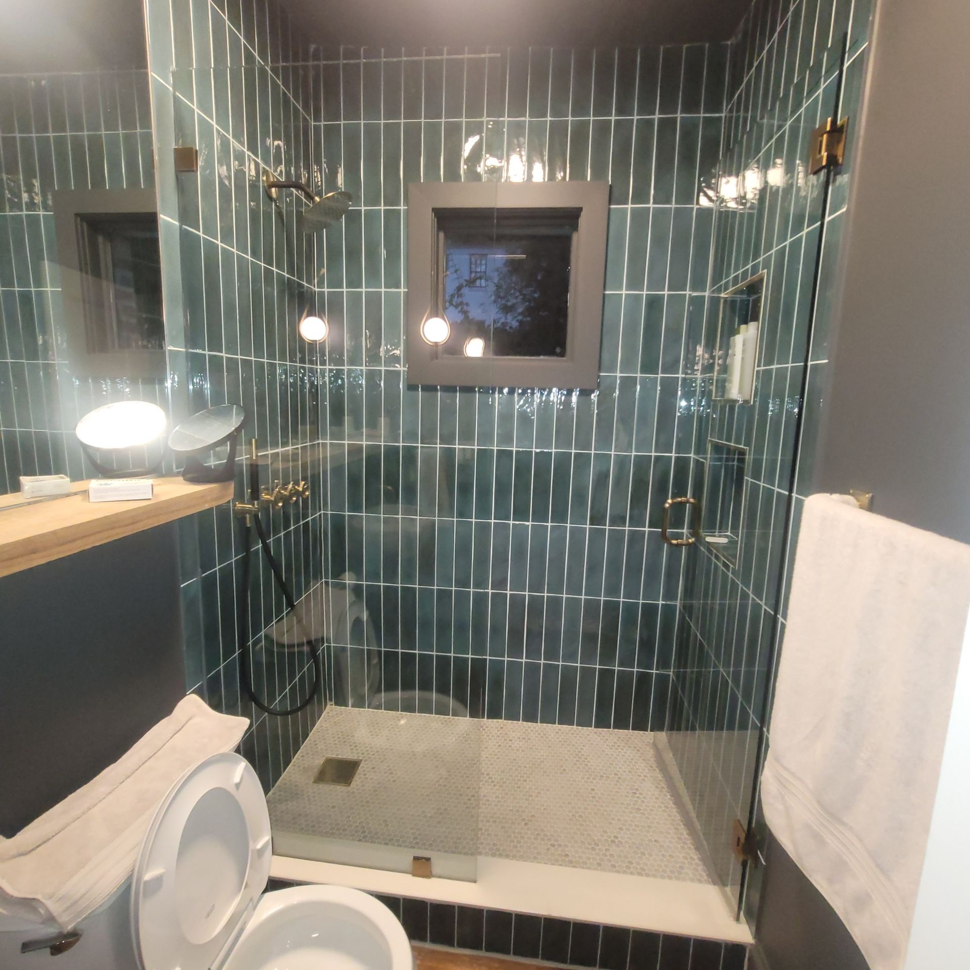 A modern bathroom with teal tile, glass shower, and toilet.