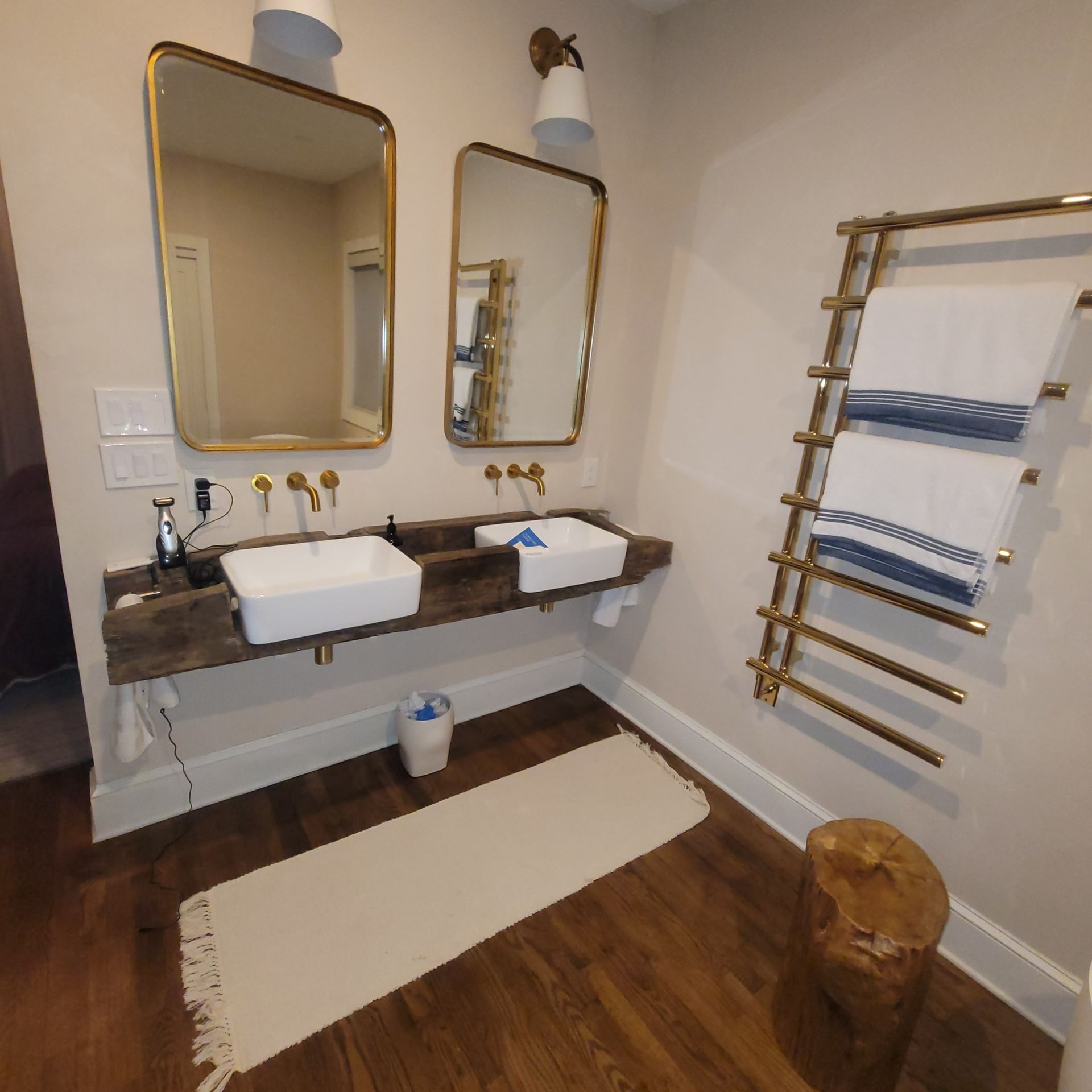 Bathroom with double sinks, gold mirrors, towel warmer, and wood accents.