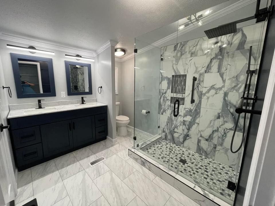 Modern bathroom with marble shower, blue vanity, and black fixtures.