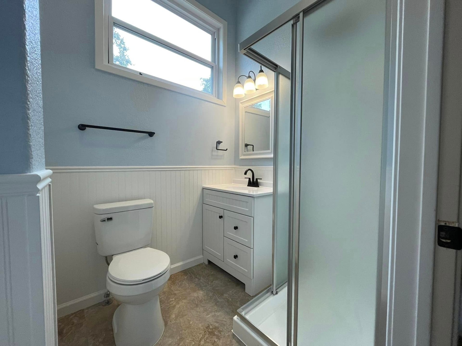Bathroom with blue walls, white vanity, toilet, and shower.