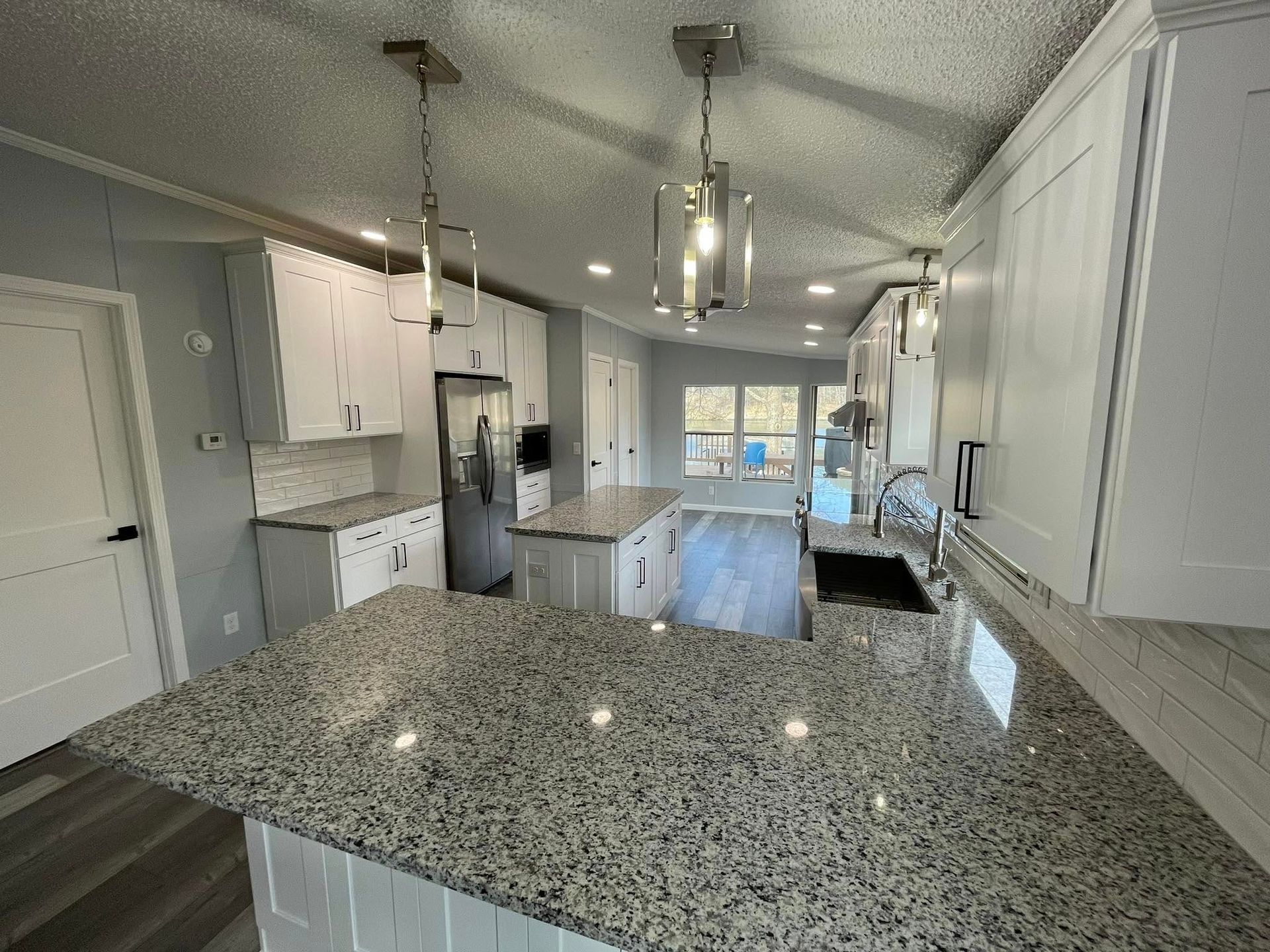 Bright kitchen with white cabinets, gray countertops, and two island pendant lights.