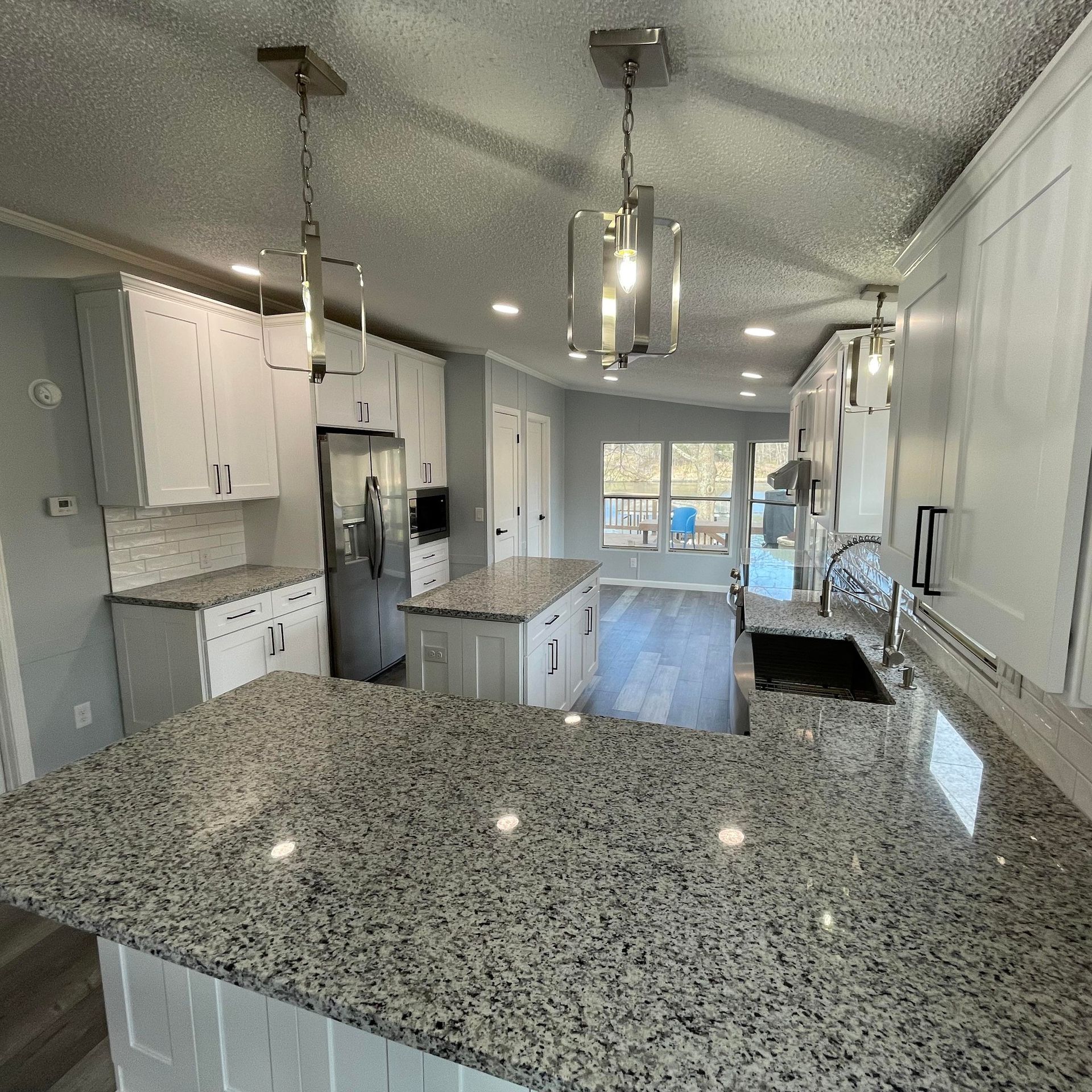 Modern kitchen with white cabinets, granite countertops, and pendant lights.