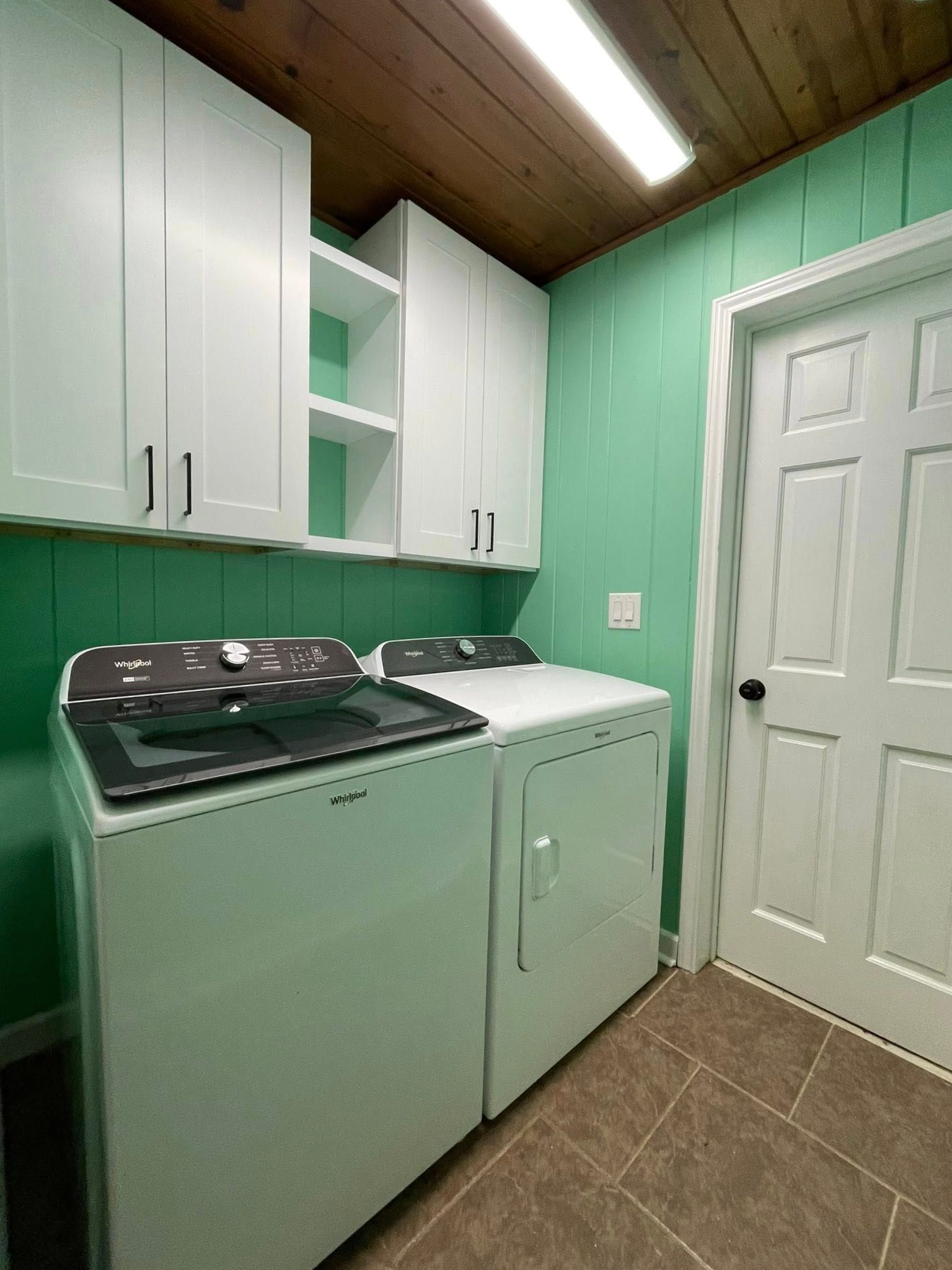 Laundry room with white appliances, cabinets, and door, green walls, brown floor.