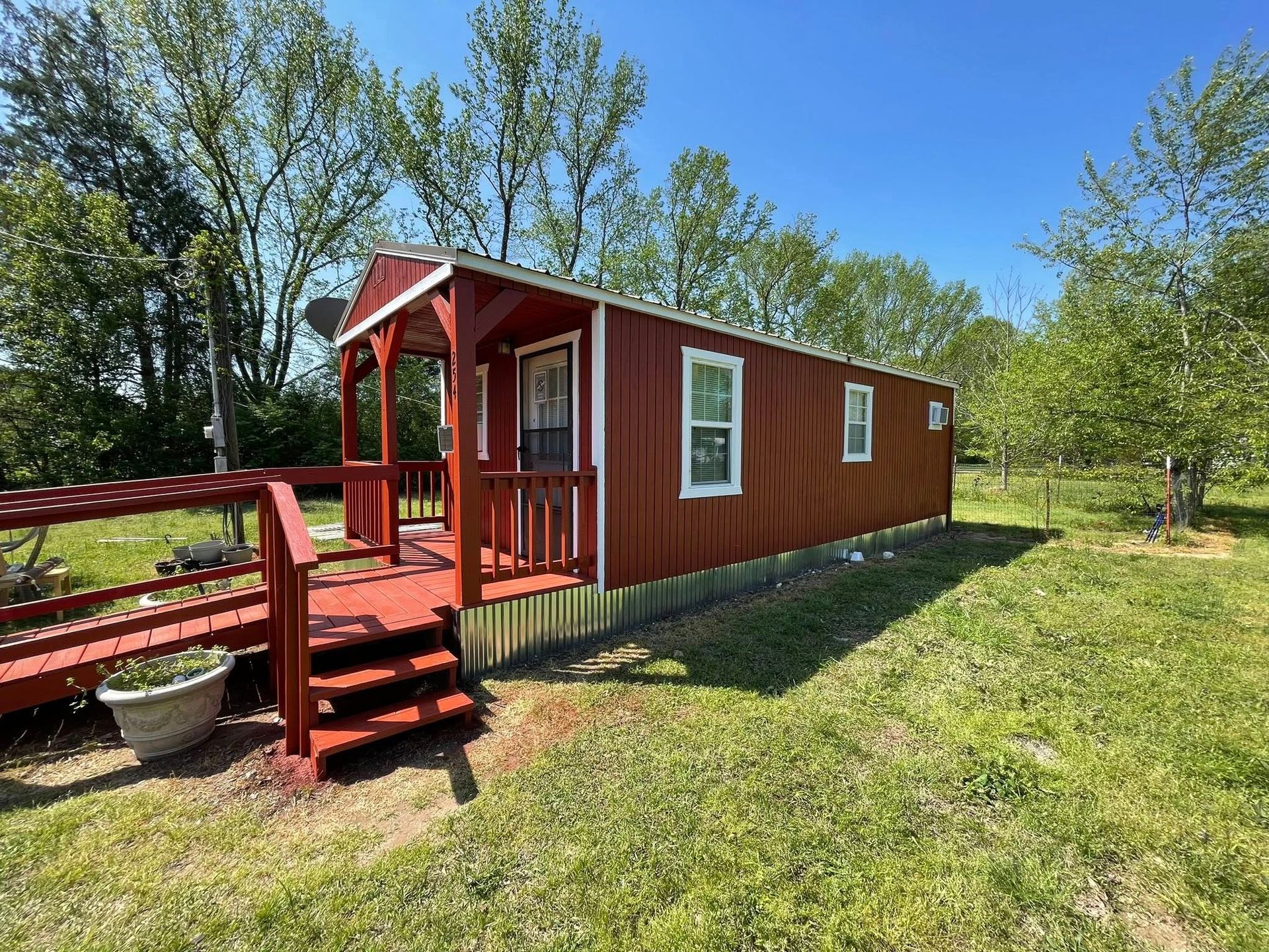 Red cabin with porch, steps, and ramp on a grassy area under a blue sky.