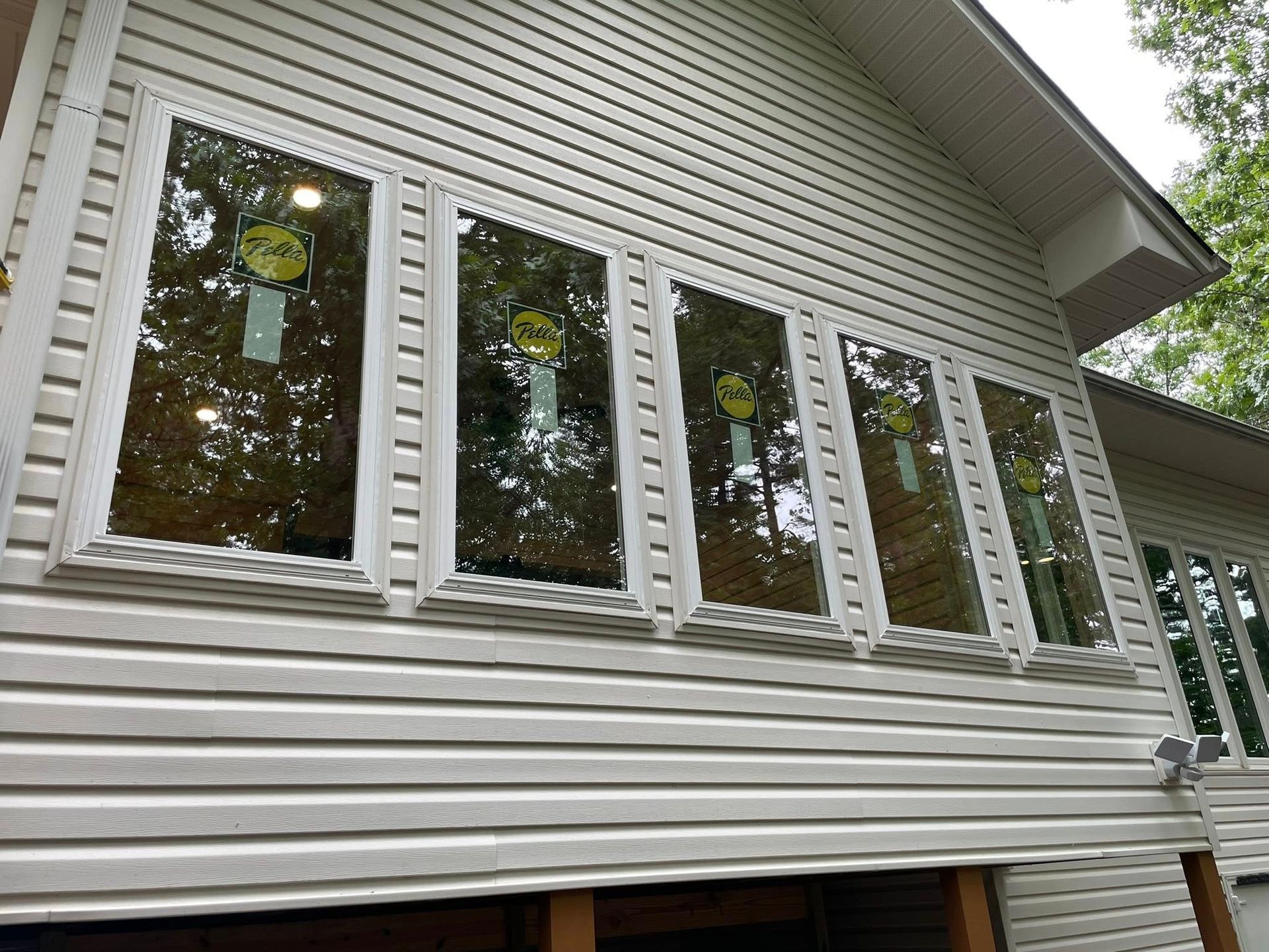 Exterior view of a house with a row of rectangular windows with reflective glass, white frames, and vinyl siding.