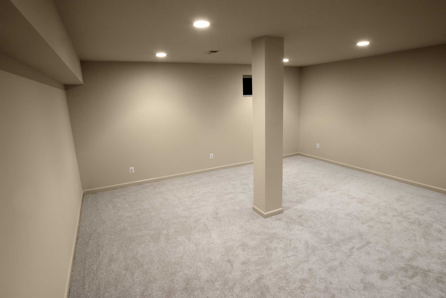 Empty basement room with light gray carpet, beige walls, and a central support column.