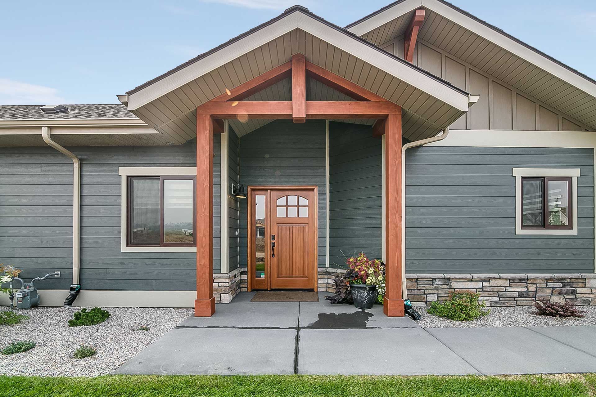 Gray house with white trim, patio, and dormer windows on a sunny day.