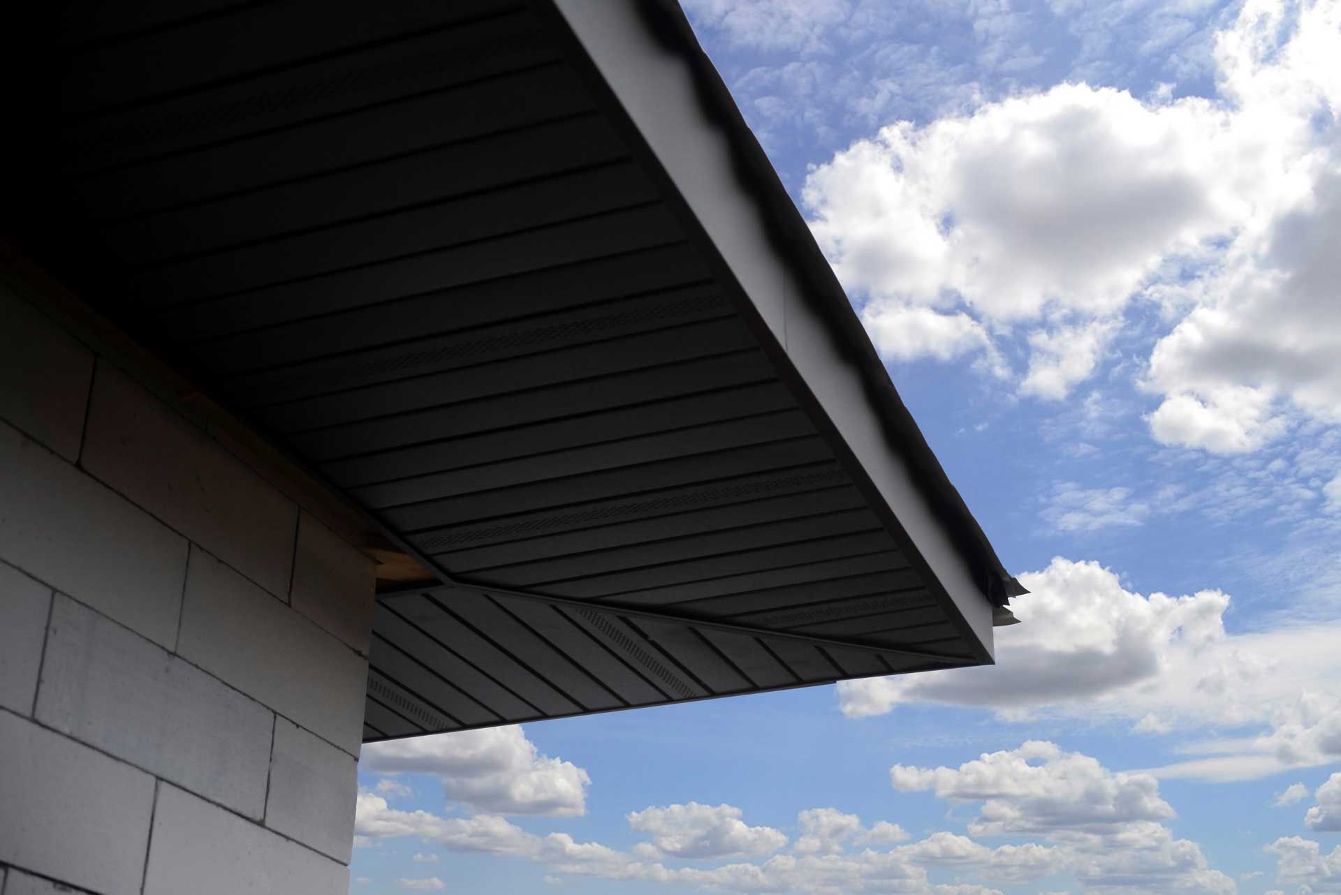Dark gray siding and eaves of a building against a blue sky with clouds.