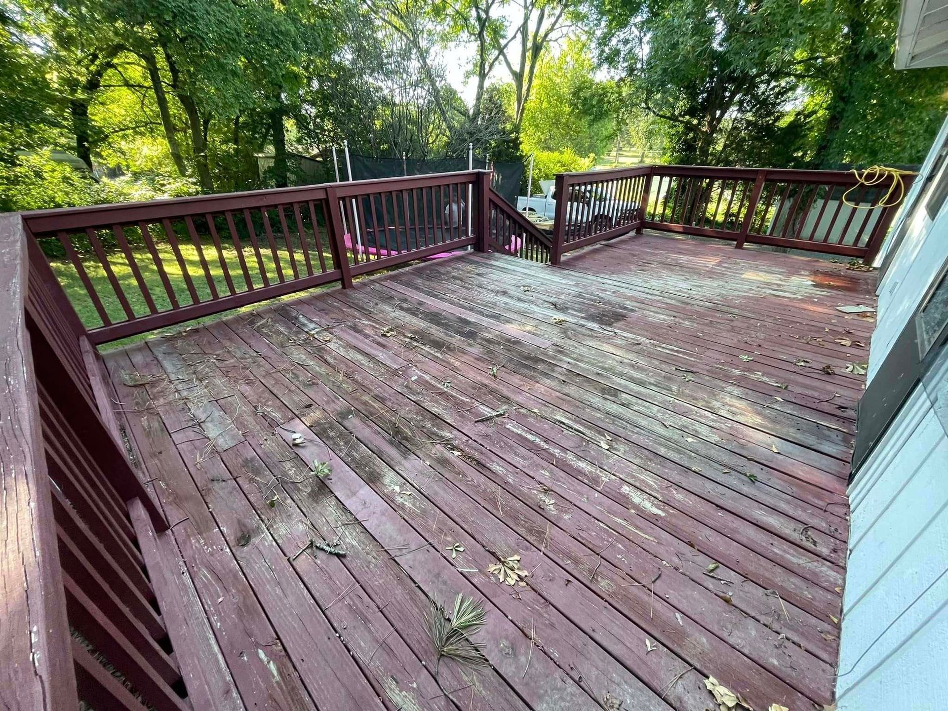 A weathered wooden deck with red railings and scattered debris, surrounded by trees.