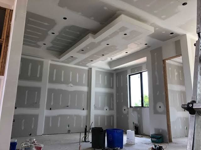 Person using a putty knife to apply white drywall compound to a tan wall.