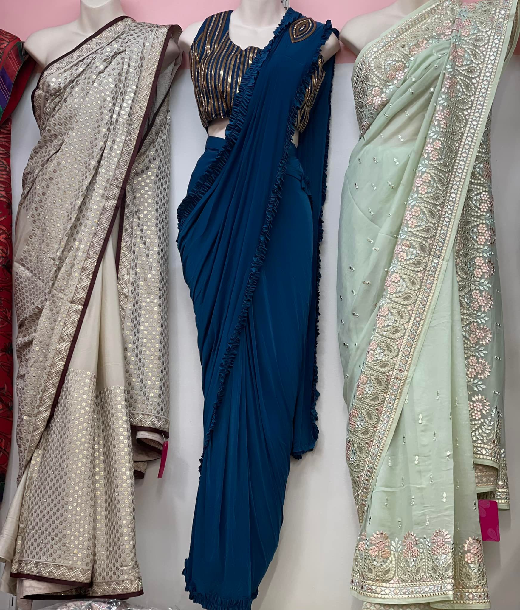 Three mannequins display ornate saris of cream, teal blue, and light green. Each is heavily embellished with sequins or embroidery.