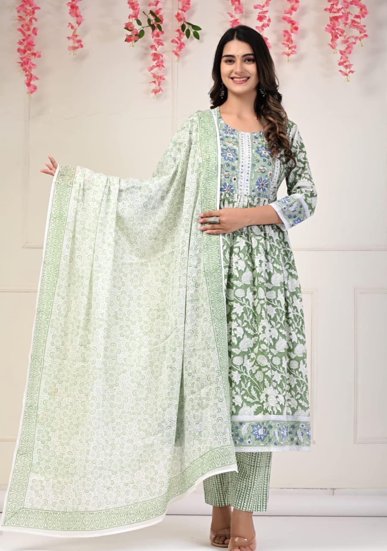Woman wearing a light green floral print Indian suit with a matching scarf. She's smiling in a bright, clean setting.