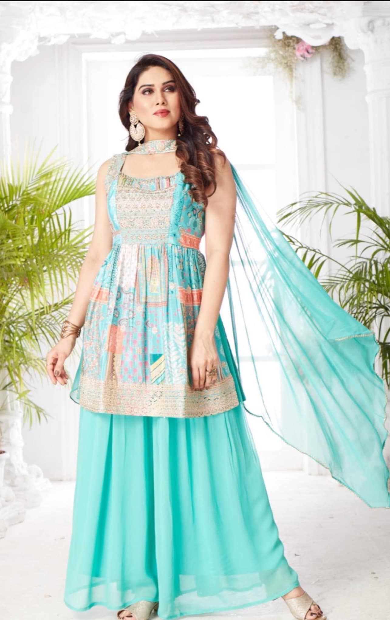 Woman in turquoise salwar kameez with matching dupatta, posing in a brightly lit room.