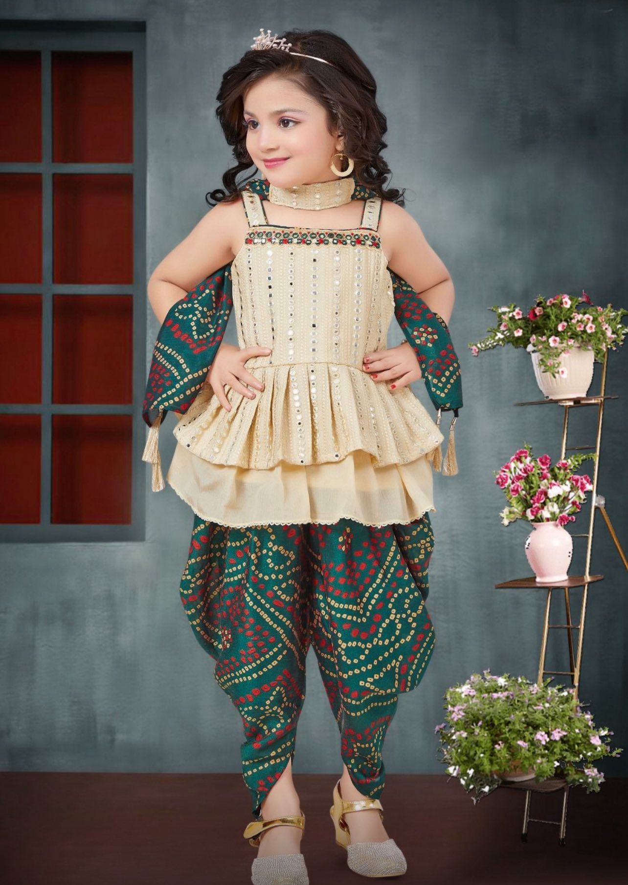 Young girl in a traditional Indian outfit with beige top, green pants, and gold accessories. Posing in a studio setting.