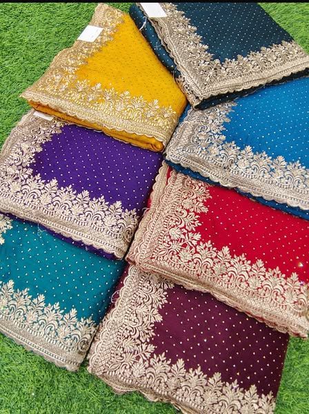Stack of colorful embroidered saris on green grass.