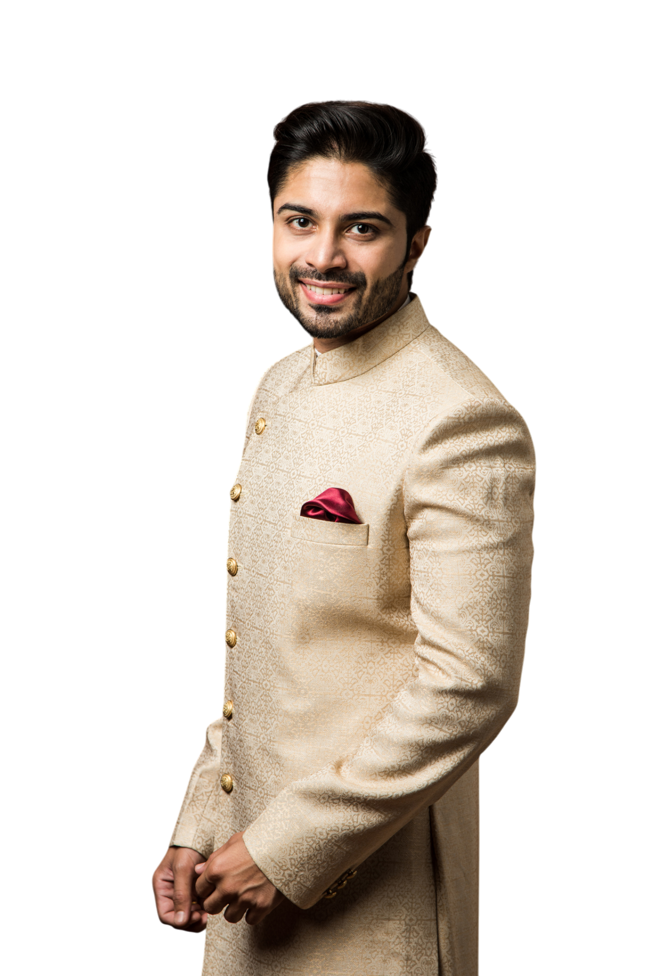 A smiling man in a beige embroidered sherwani, with a burgundy pocket square, stands against a white background.