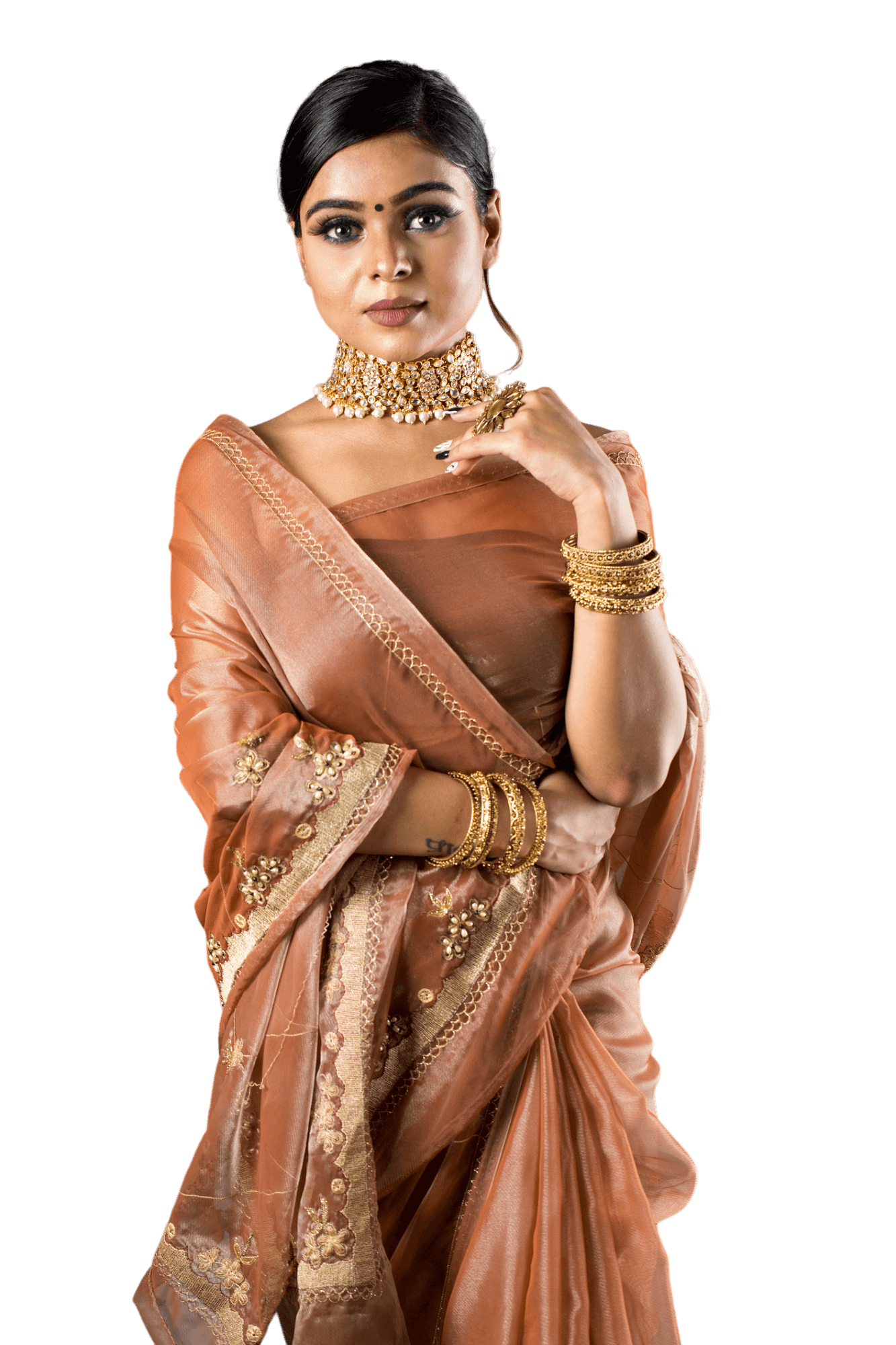 Woman in a brown sari and gold jewelry, with her hand near her face. She is looking at the camera.