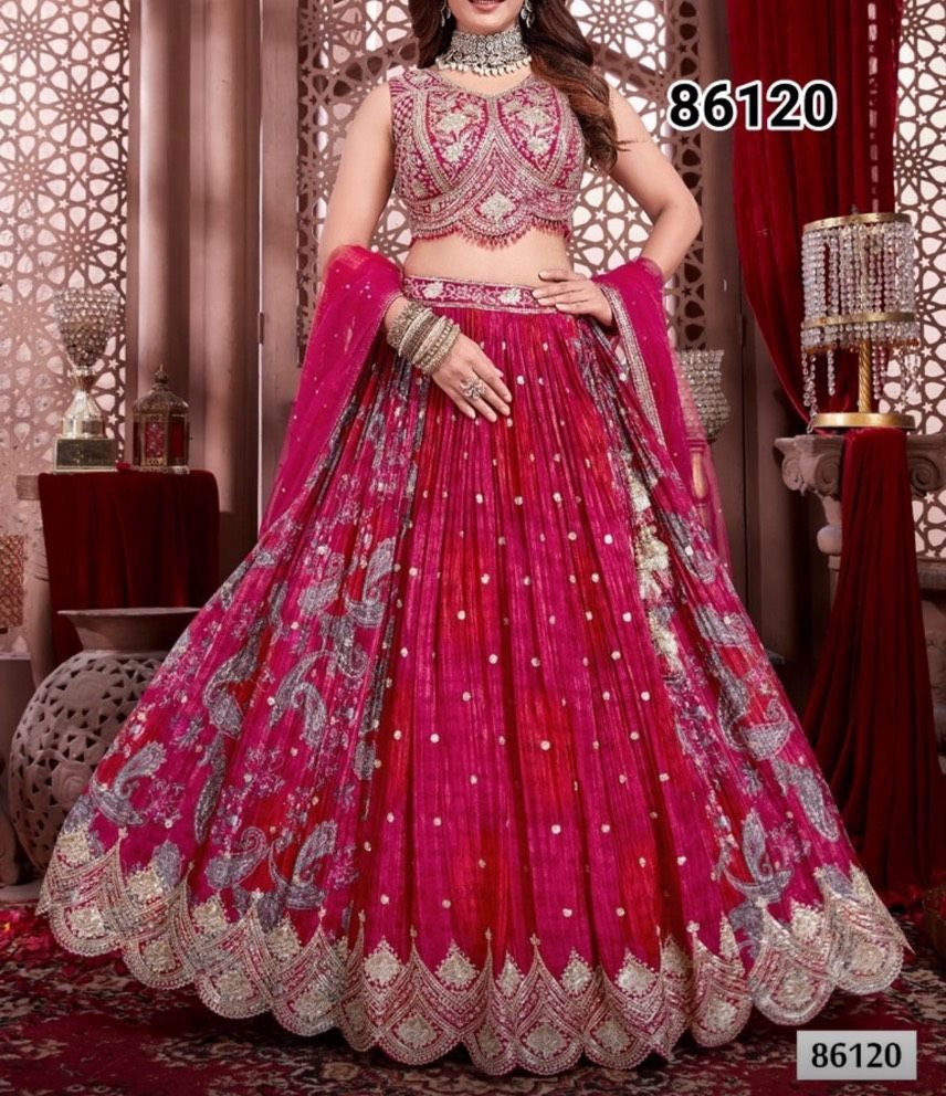 Woman in a pink embroidered lehenga. She's in a decorated room with red curtains, holding a matching dupatta.