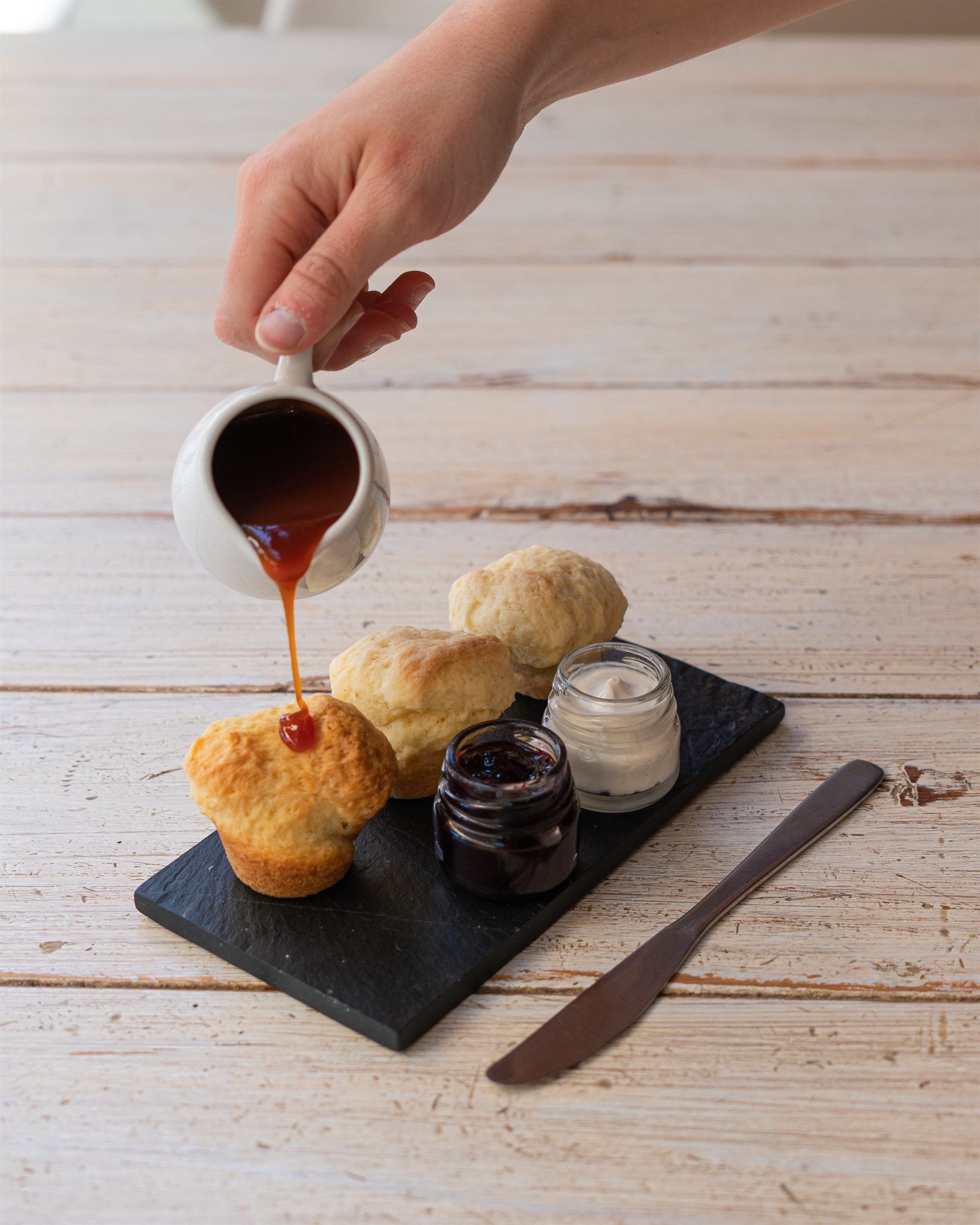 Una persona está vertiendo jarabe sobre un panecillo en una tabla de cortar.