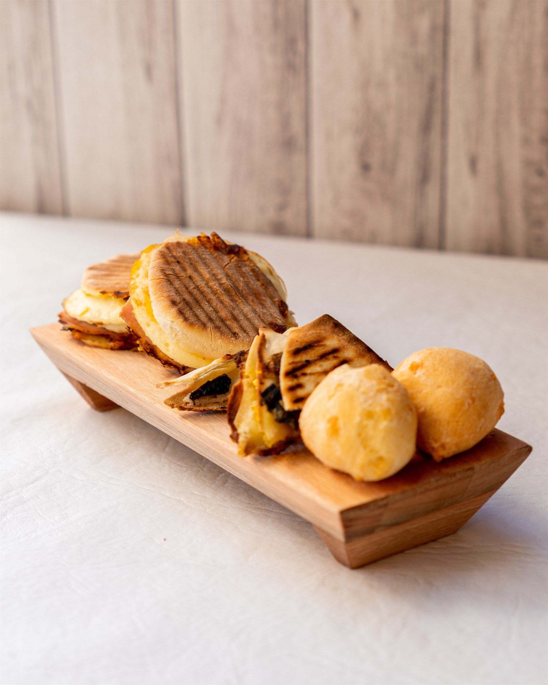 Una bandeja de madera llena de pan y sándwiches sobre una mesa.