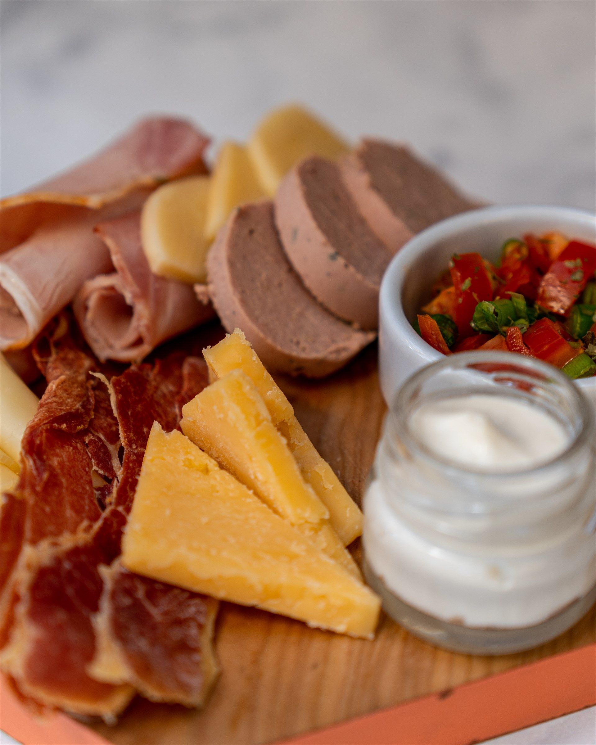 Una tabla de cortar de madera cubierta con carne, queso y salsa.