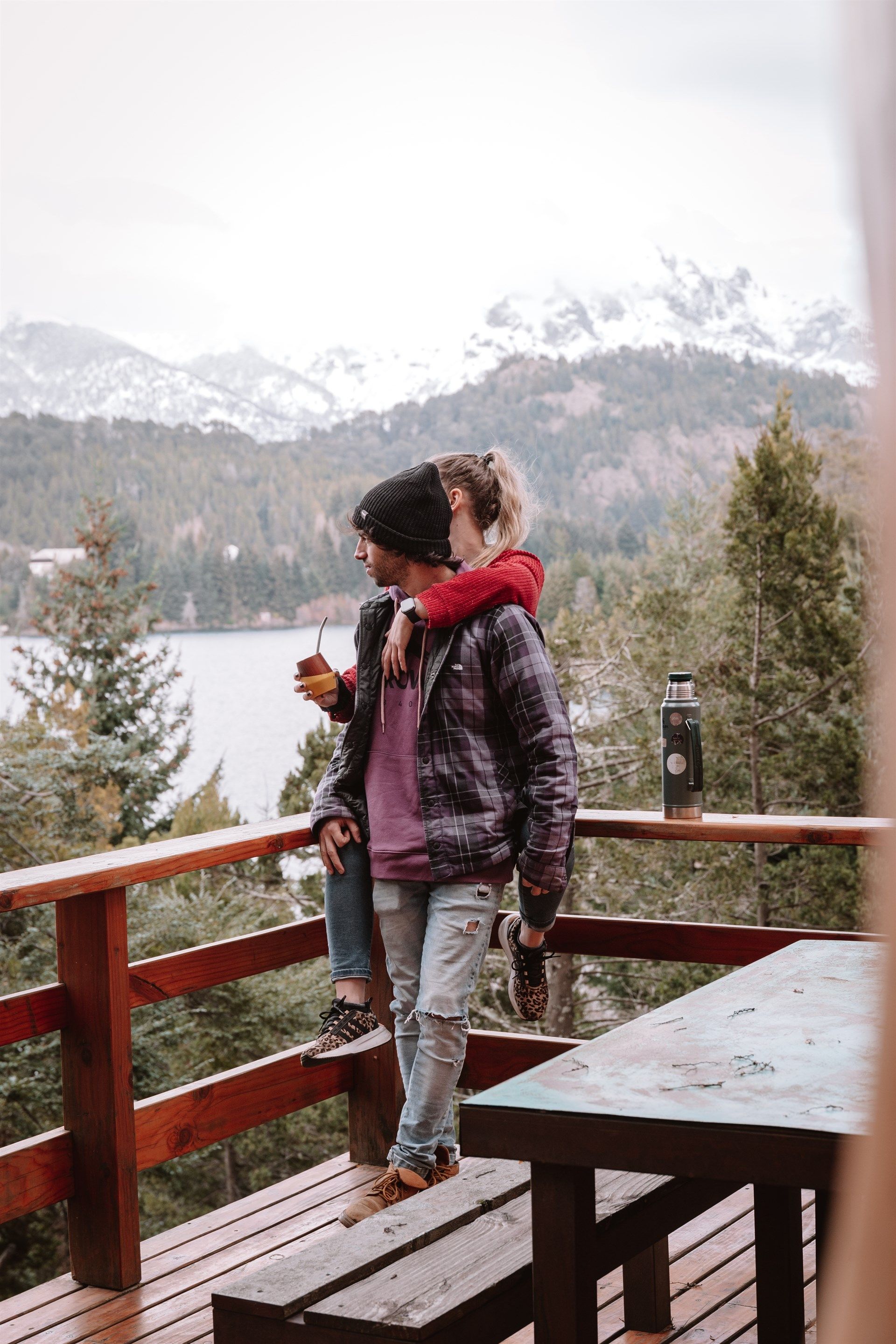 Un hombre y una mujer están sentados en una terraza de madera con vistas a un lago.