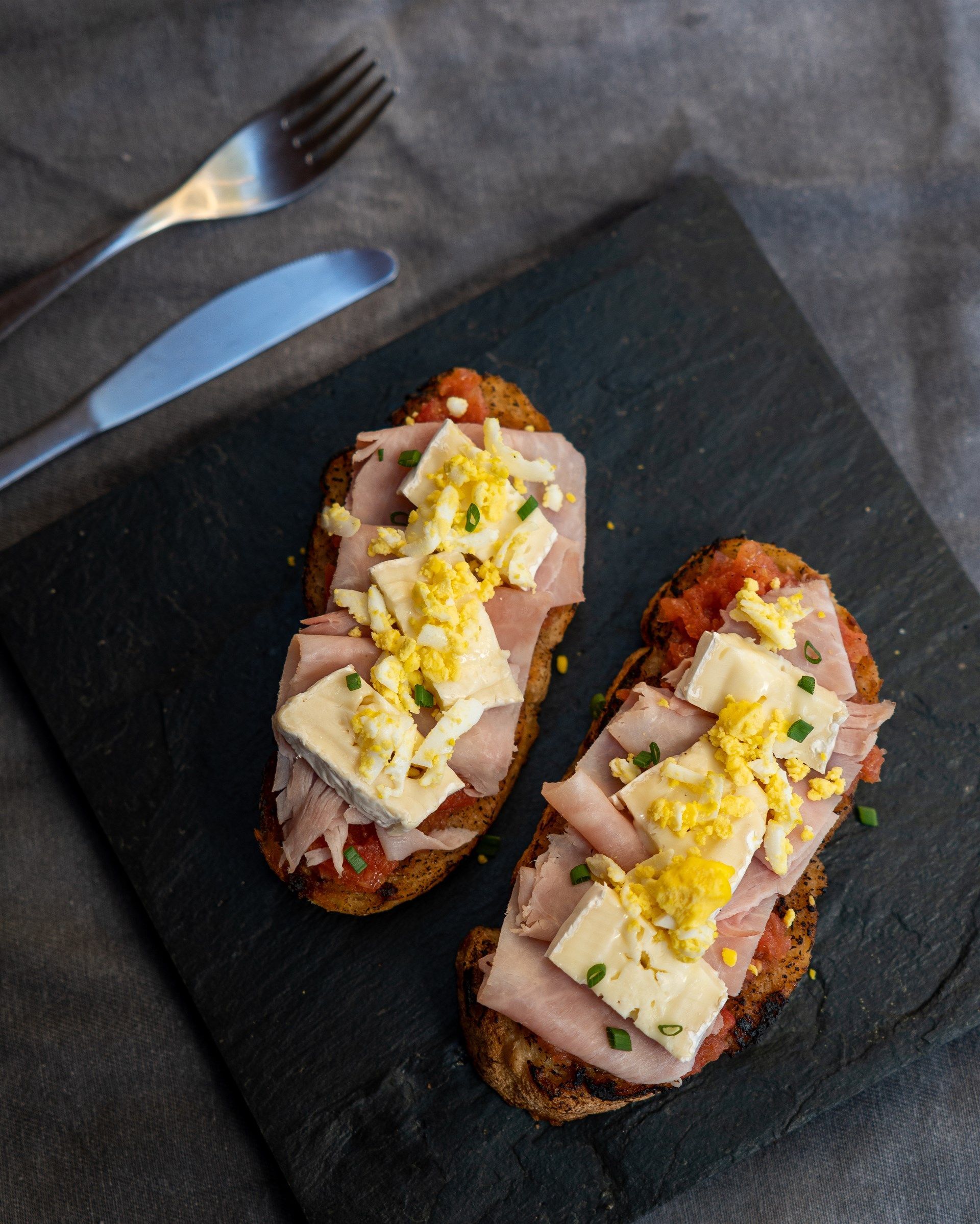 Dos sándwiches con jamón, queso, huevos y tomates en un plato negro.